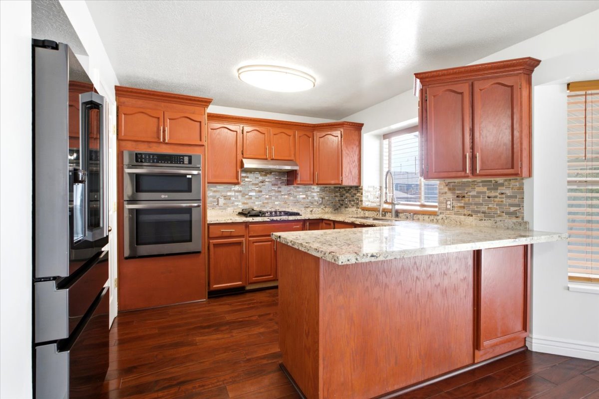Kitchen featuring rich wood cabinetry, stone countertops, a tile backsplash, stainless steel appliances, and wood-finish flooring