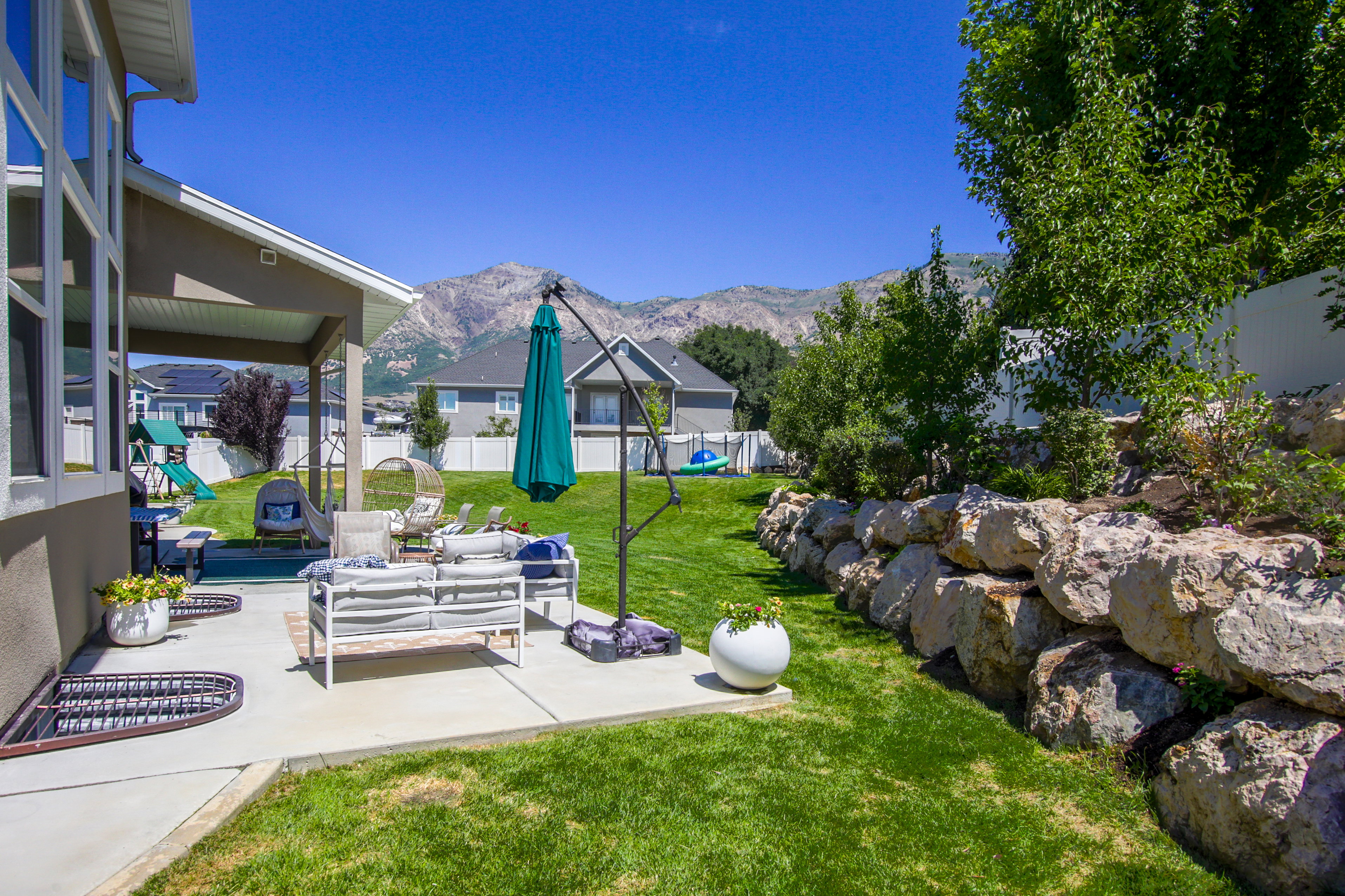Expansive backyard featuring a covered patio, manicured lawn, and a natural rock retaining wall
