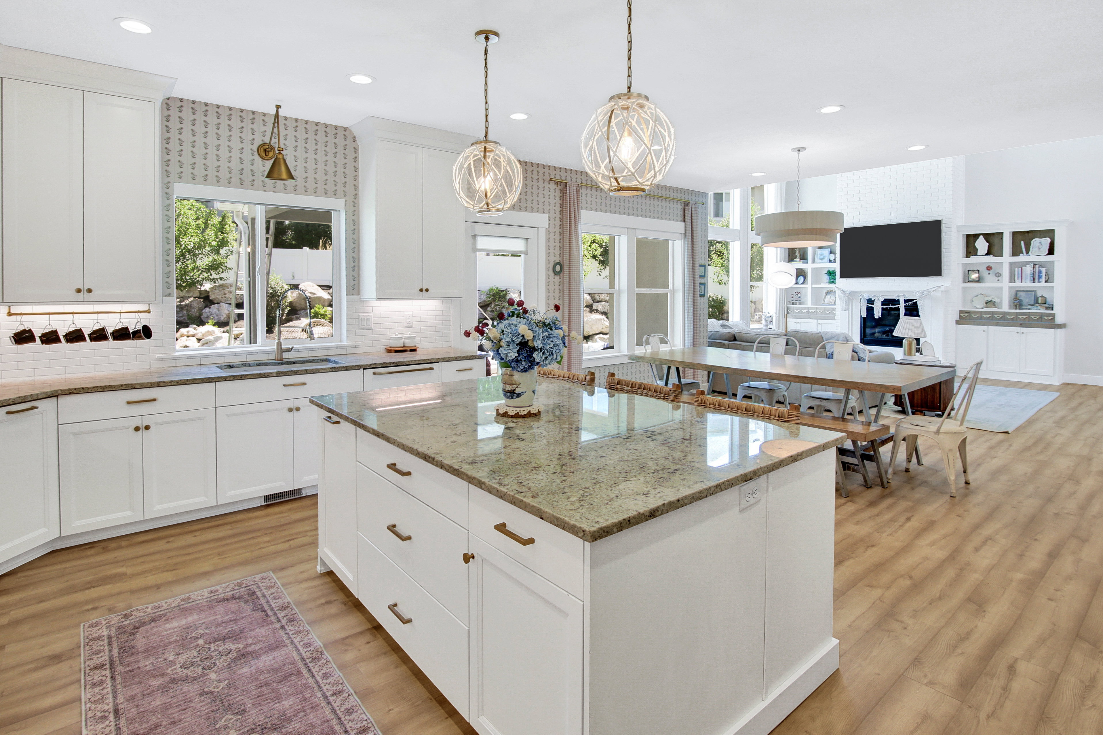 Open-concept kitchen and living area featuring a large center island with stone-finish countertop, white cabinetry with bronze hardware, wood-finish flooring, and two modern spherical pendant lights