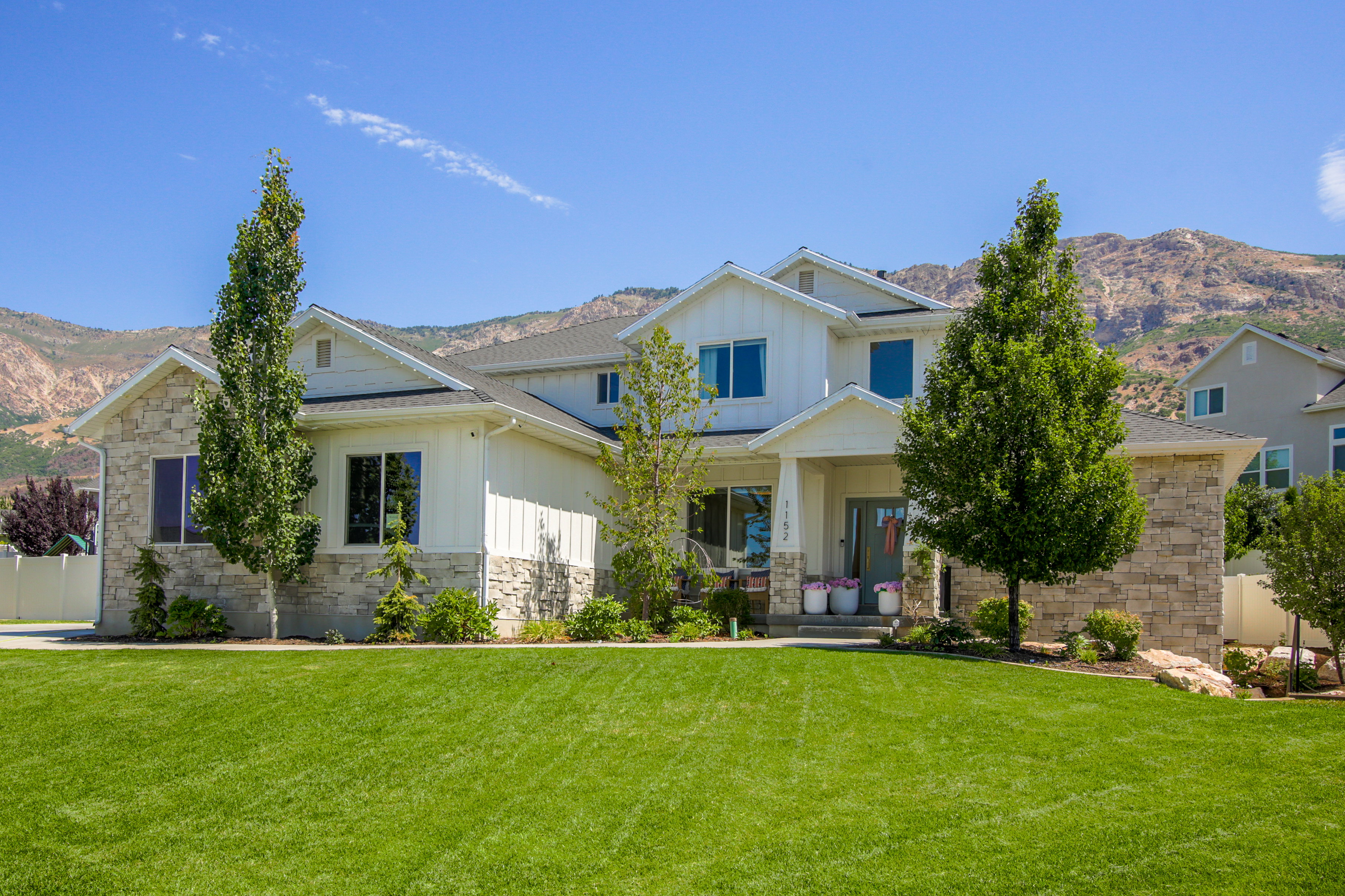 Two-story residence featuring a stone and board and batten facade, a covered front porch, and a professionally landscaped front yard with a lush green lawn
