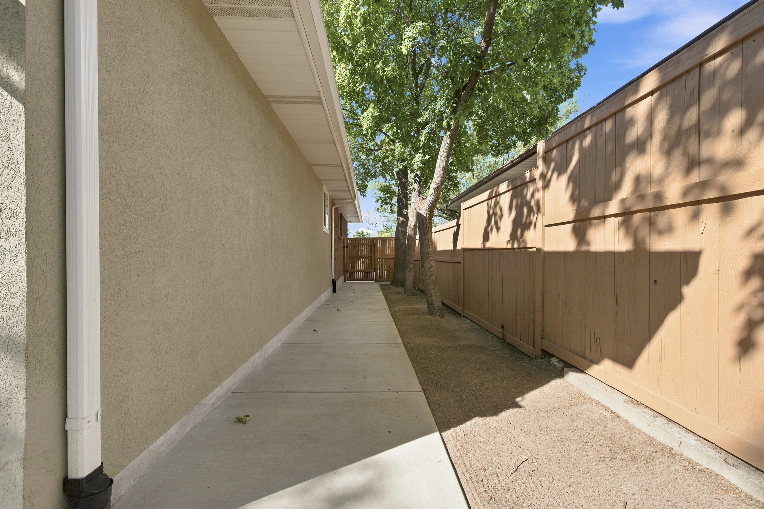 Concrete pathway alongside a stucco exterior wall with white rain gutter