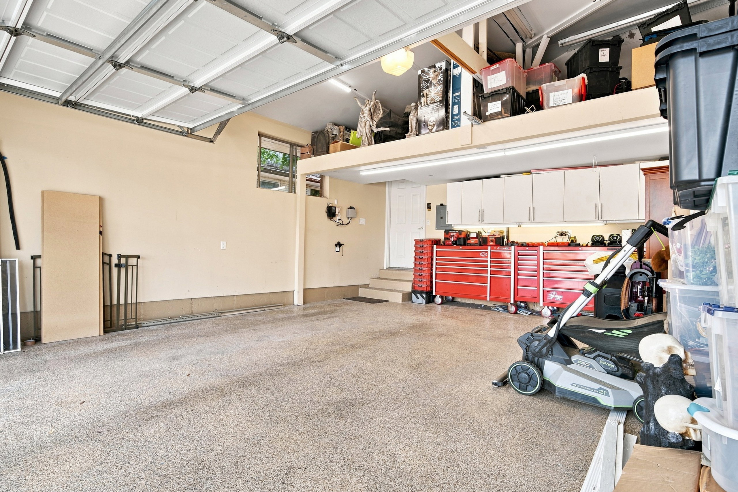 Spacious garage featuring a durable epoxy-coated floor, overhead door, built-in cabinetry, and a dedicated storage loft