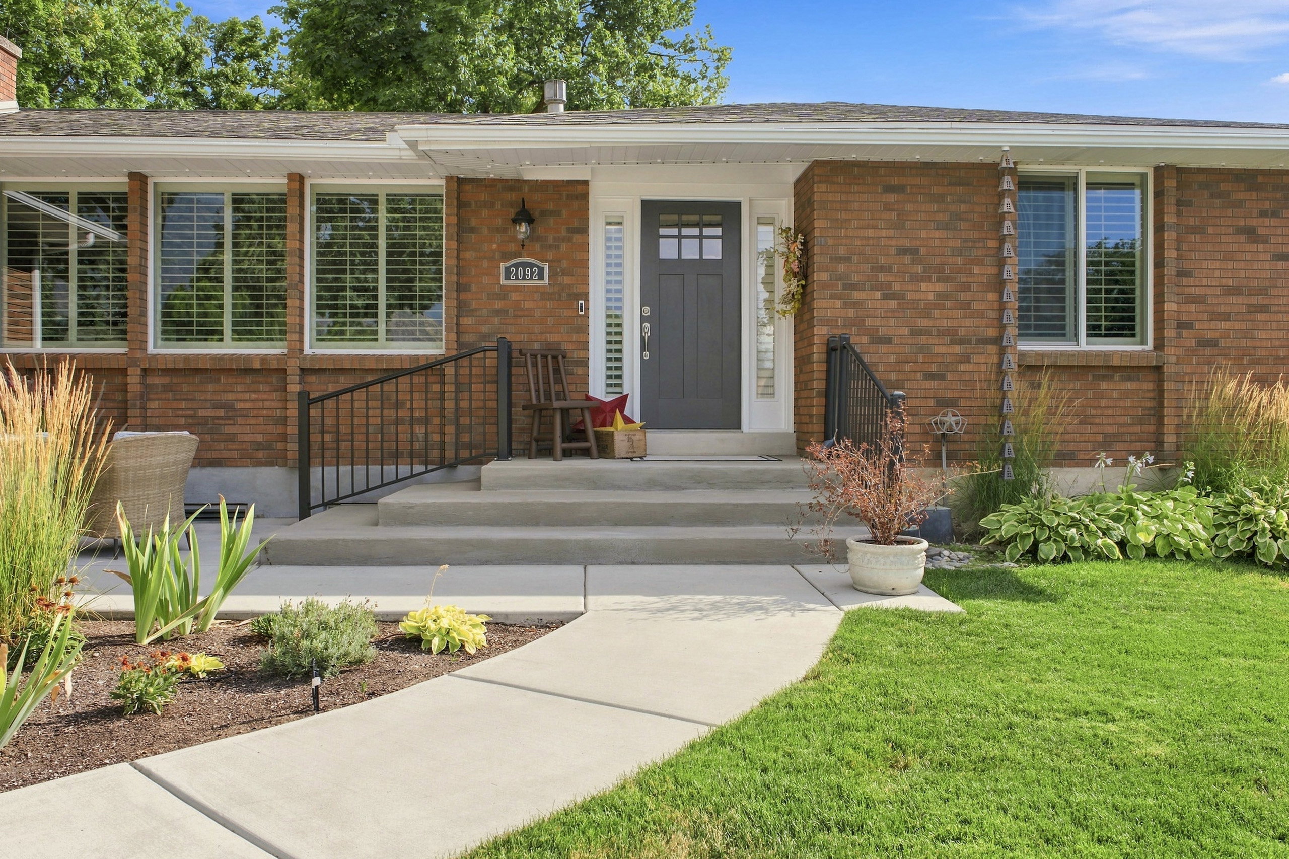Brick exterior featuring a dark gray paneled entry door with transom window, concrete steps, and a black wrought iron railing