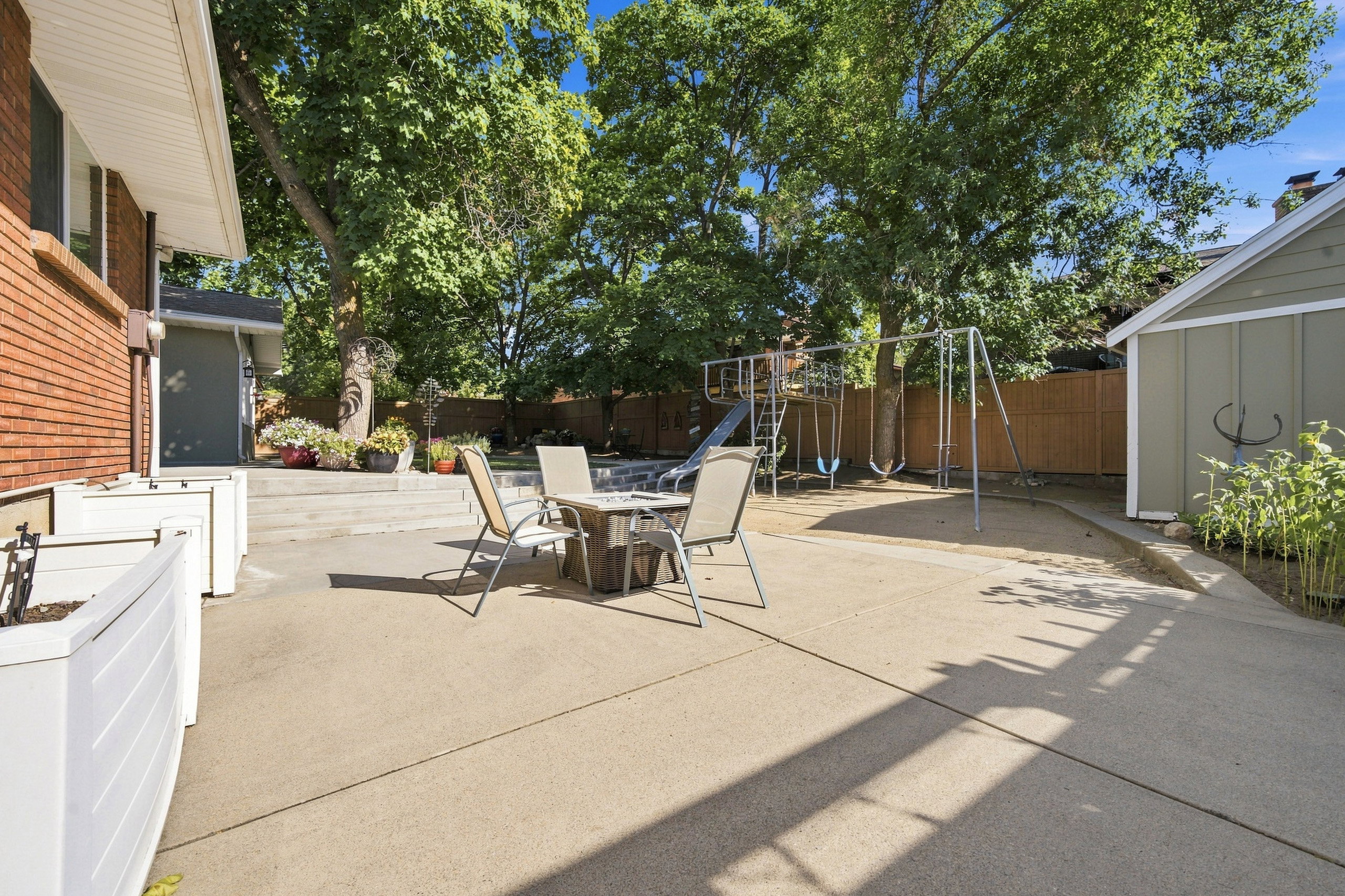 Expansive concrete patio area featuring multiple levels, white planter boxes, and mature trees providing shade