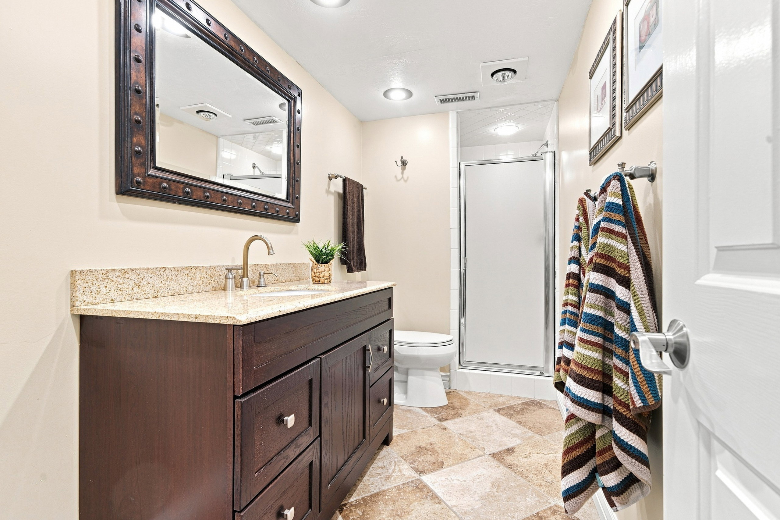 Bathroom featuring a dark wood-finish vanity with a light speckled countertop, under-mount sink, and a framed mirror