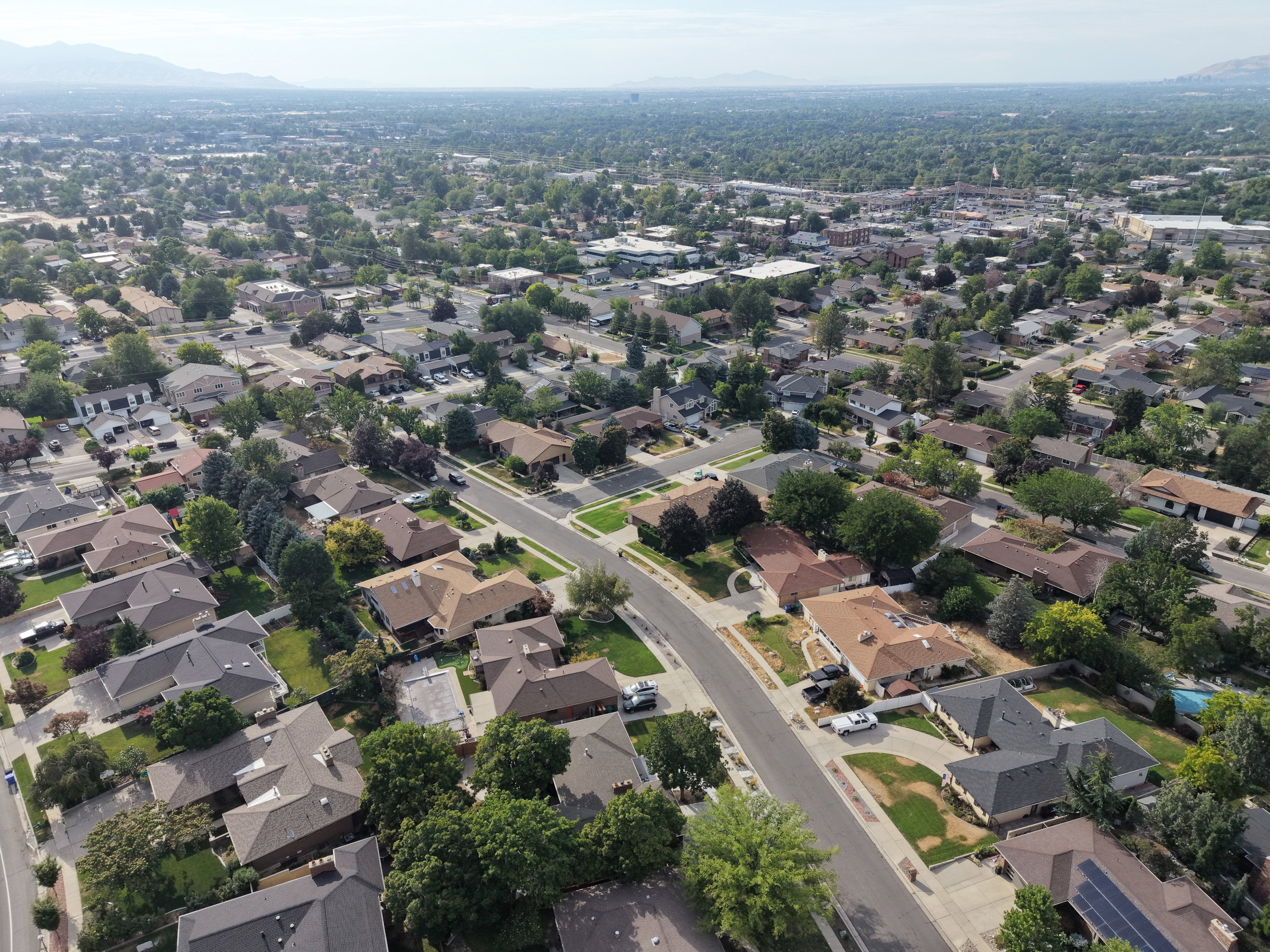 Aerial perspective showcasing a residential neighborhood with varied rooflines and established tree cover, set against a distant mountain range