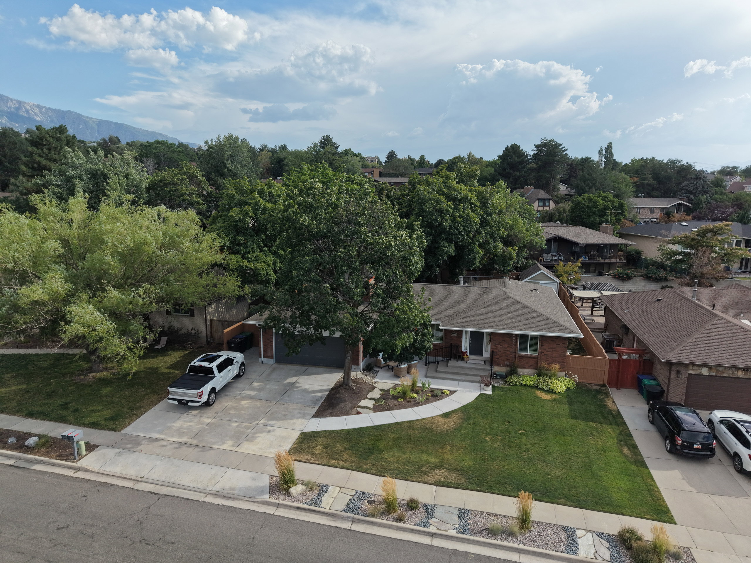 Brick ranch-style residence featuring a prominent front lawn, established landscaping, a concrete driveway, and an attached garage