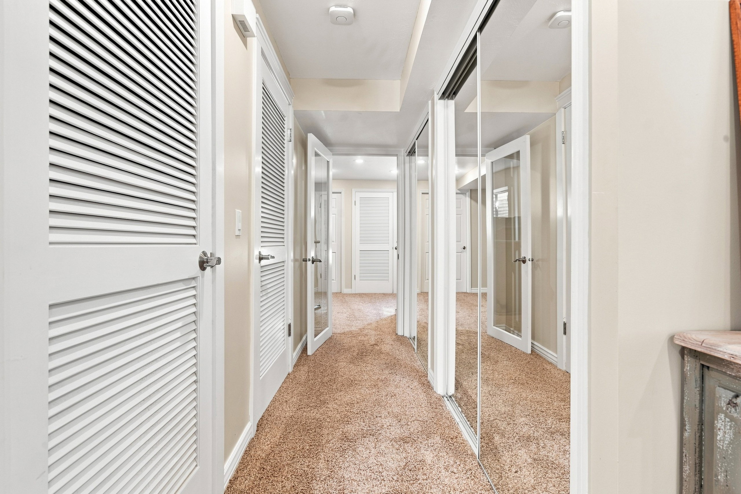 Hallway featuring light-toned carpeting, louvered doors, mirrored closet doors, and recessed lighting
