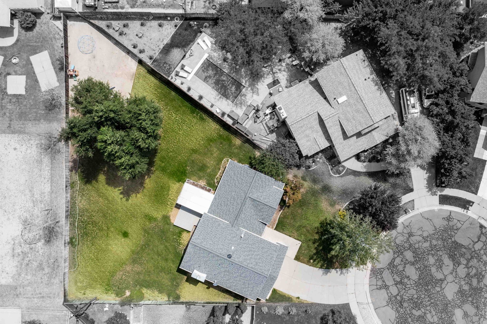 Expansive green lawn surrounds the property, featuring mature trees and a paved driveway leading to the residence