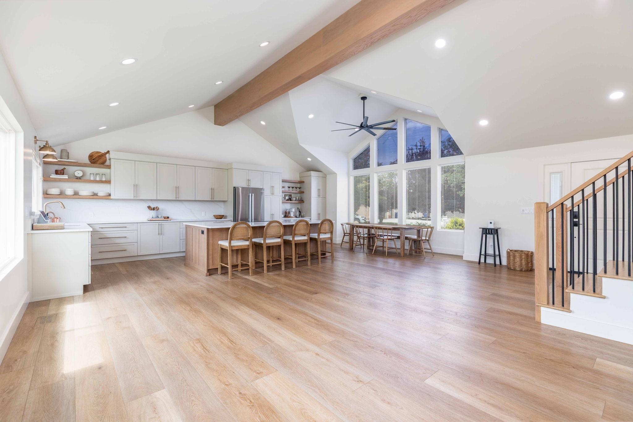Spacious open-concept living area featuring wood-finish flooring, a vaulted ceiling with a visible beam, and recessed lighting