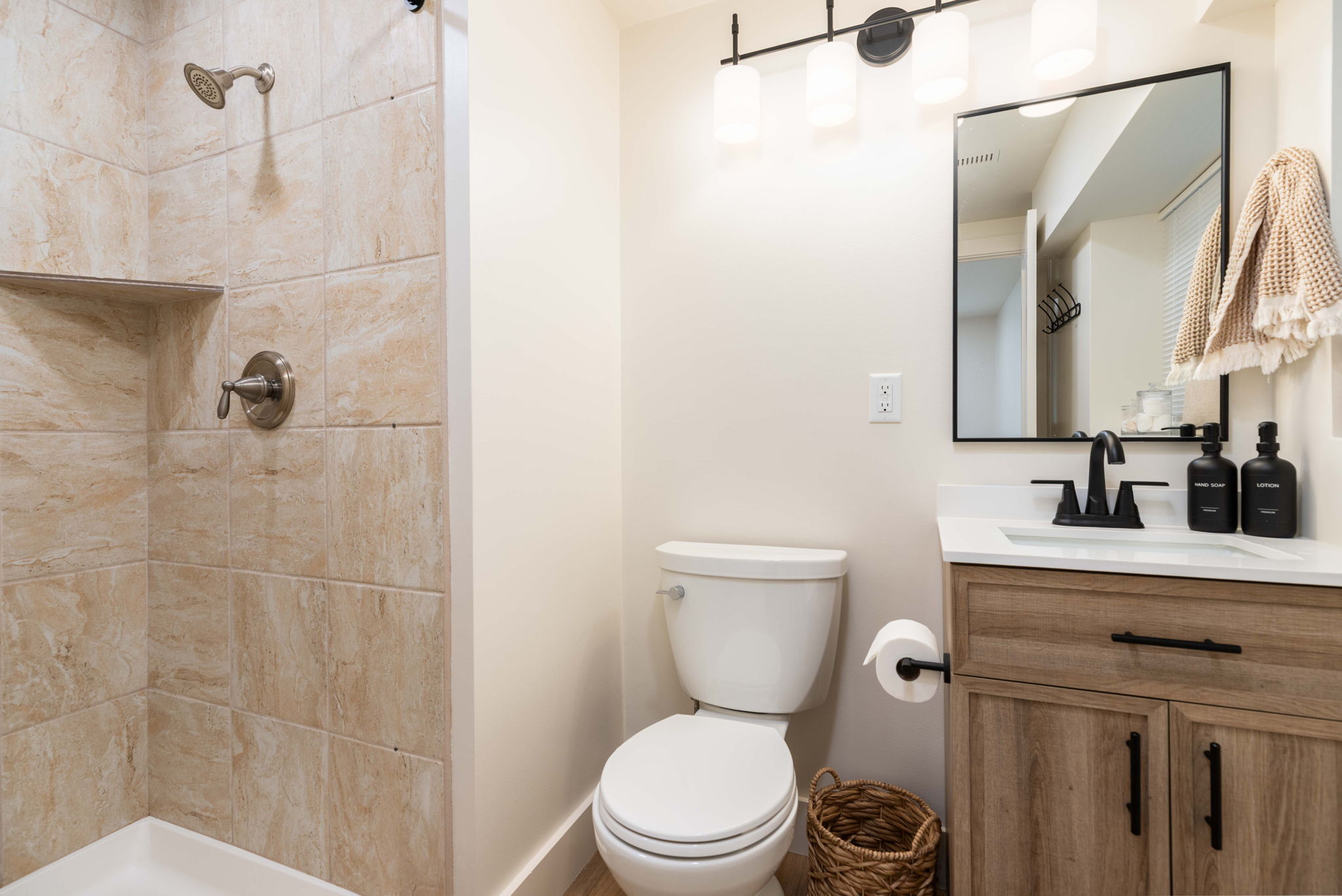Bathroom featuring a walk-in shower with tiled walls and a built-in shelf, a toilet, and a vanity with wood-finish cabinetry, a white countertop, and a black-framed mirror