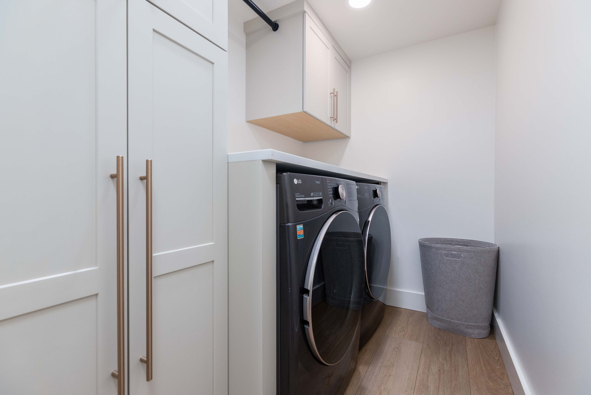 Dedicated laundry area featuring a white countertop, light wood-finish flooring, and shaker-style cabinetry with long metallic pulls