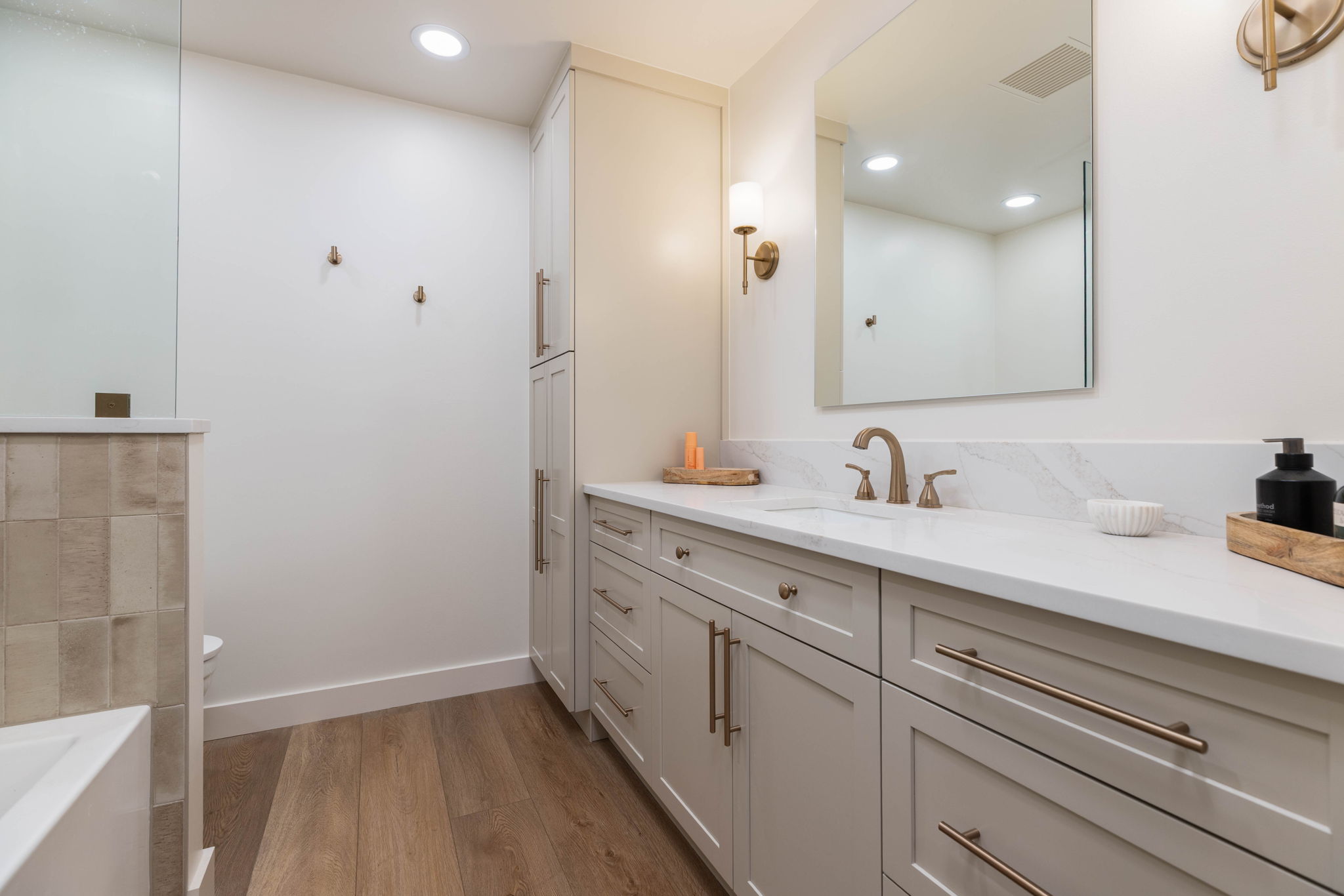 Spacious bathroom featuring a double vanity with stone countertops, integrated sink, and modern cabinetry with brushed bronze hardware