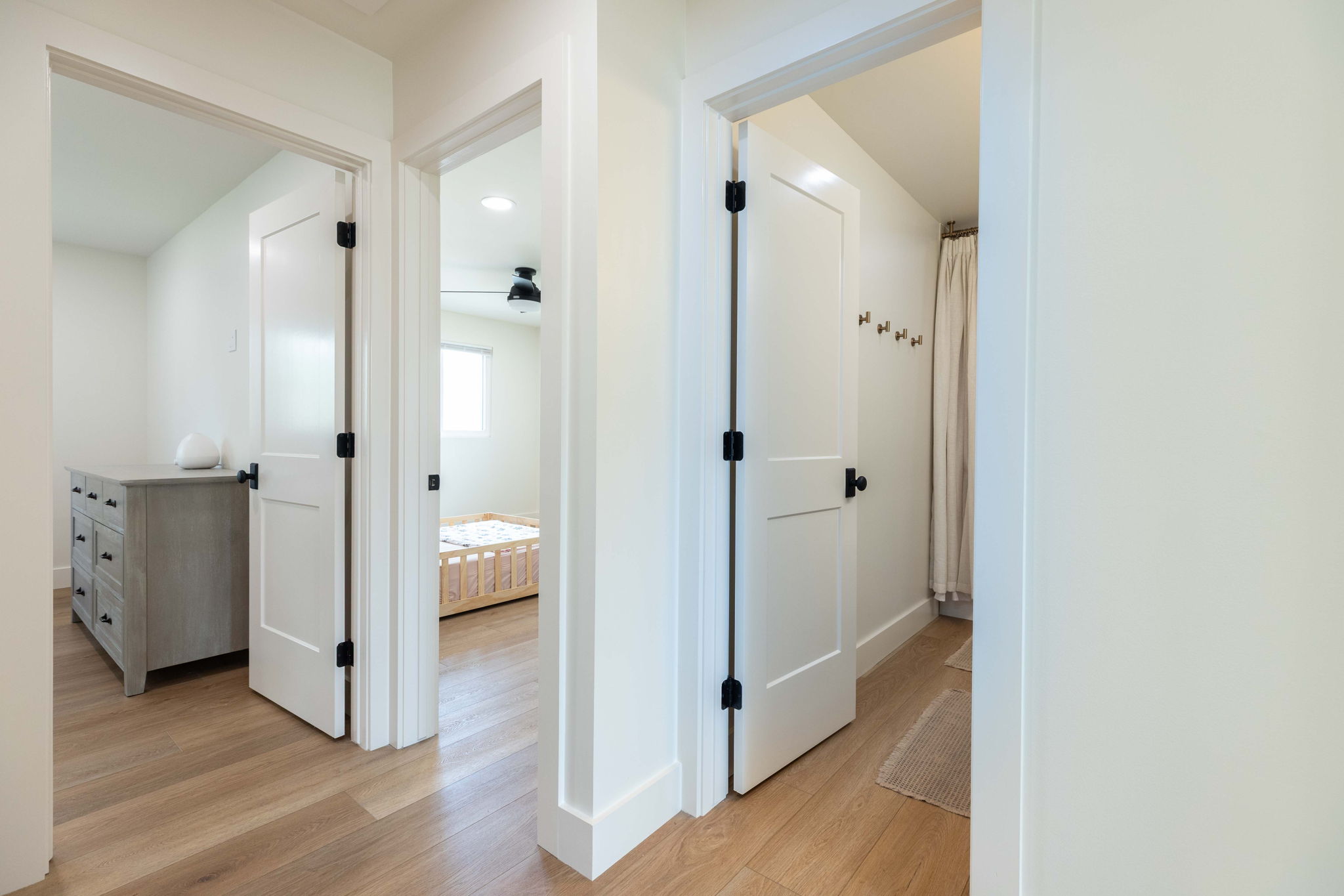 Hallway featuring wood-finish flooring, white paneled doors with matte black hardware, and crisp white baseboards