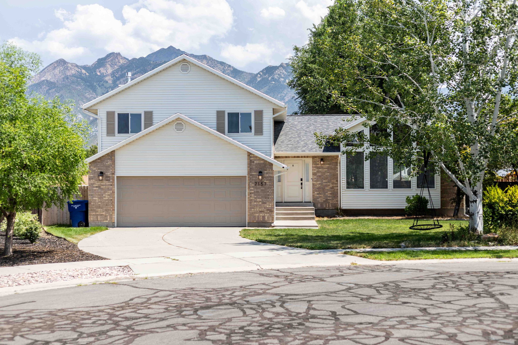 Two-story traditional residence with mountain backdrop, featuring a two-car garage, brick and siding exterior, established front landscaping, and a pitched roof