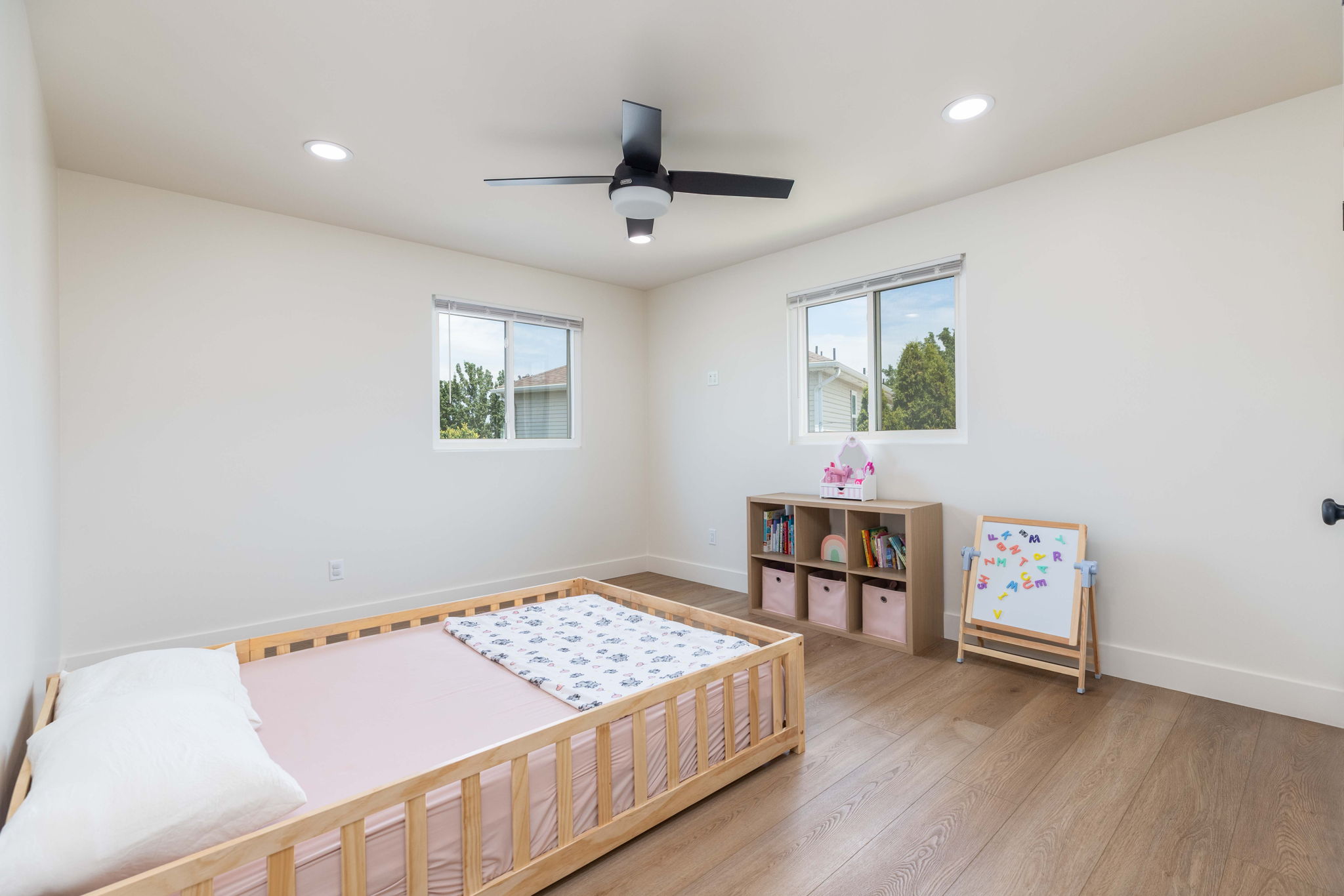 Spacious room featuring wood-finish flooring, white walls, and a black ceiling fan with integrated lighting