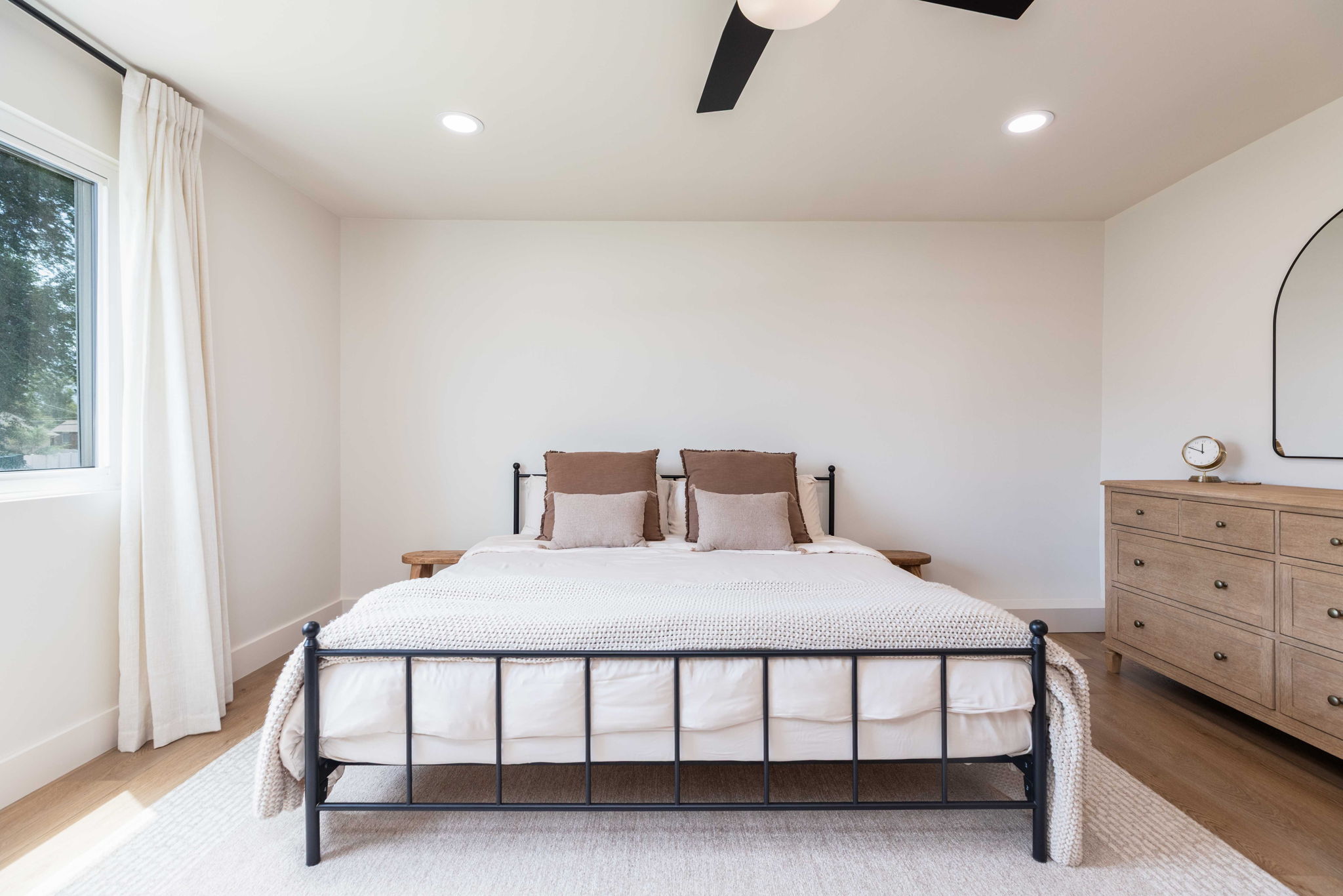Recessed lighting illuminates this room featuring wood-finish flooring, a contemporary ceiling fan, and a large window with roller shades