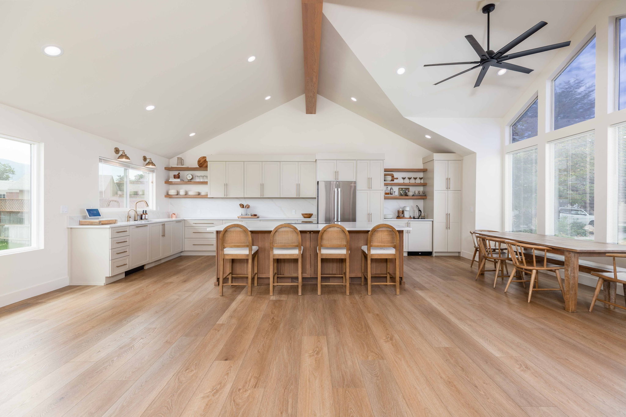 Open-concept living space featuring vaulted ceilings with exposed wood beams, wood-finish flooring, a kitchen island with seating, a full suite of stainless steel appliances, and expansive windows