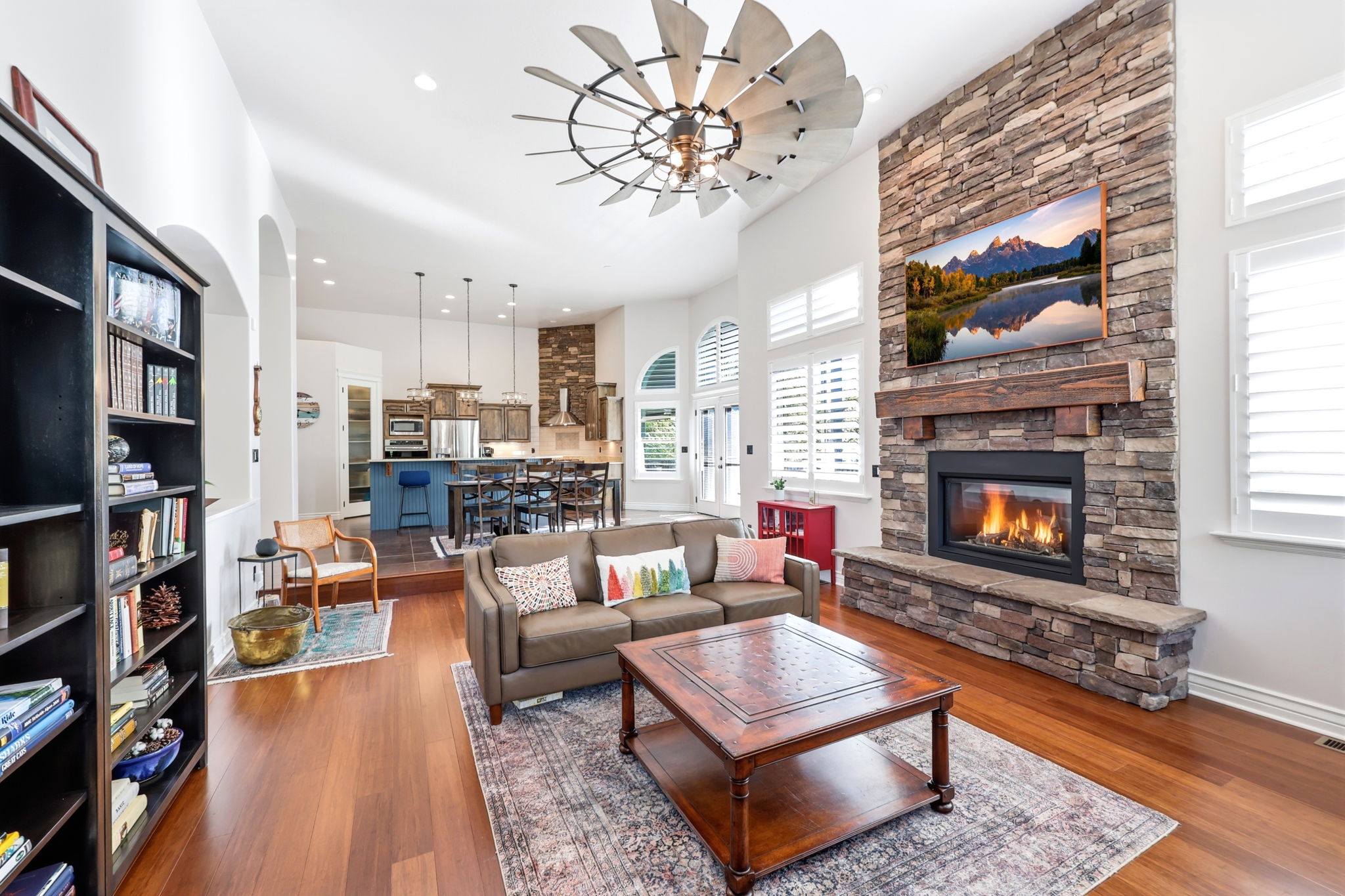 Living area featuring a stone fireplace with a wood mantle, high vaulted ceilings, wood-finish flooring, and a large built-in shelving unit