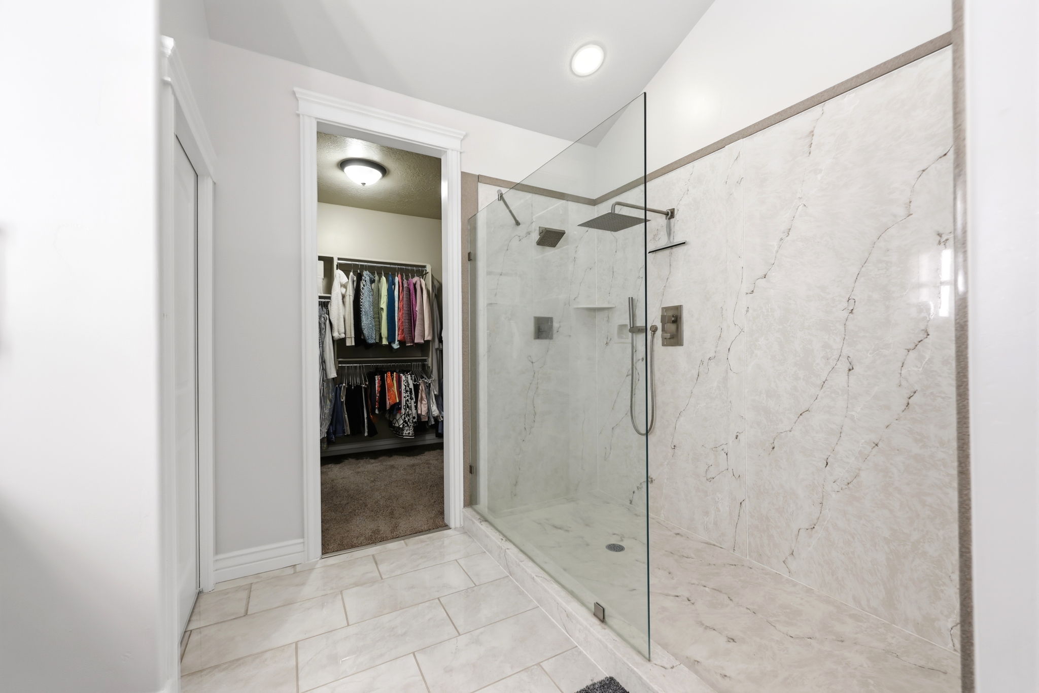 Spacious walk-in shower featuring large format veined wall tiles, a frameless glass enclosure, and multiple showerheads