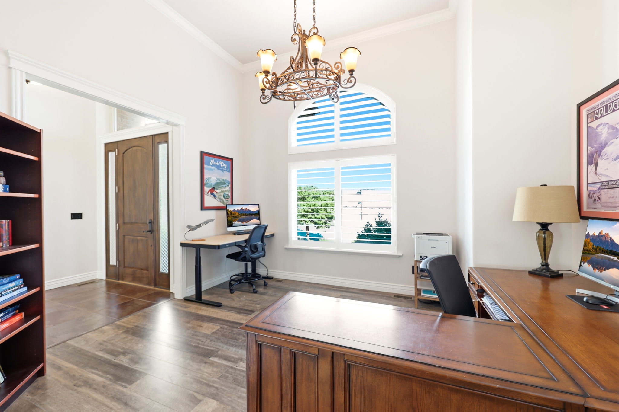Office space featuring a double-arched window with plantation shutters, wood-finish flooring, a decorative chandelier, and a substantial wood-paneled desk