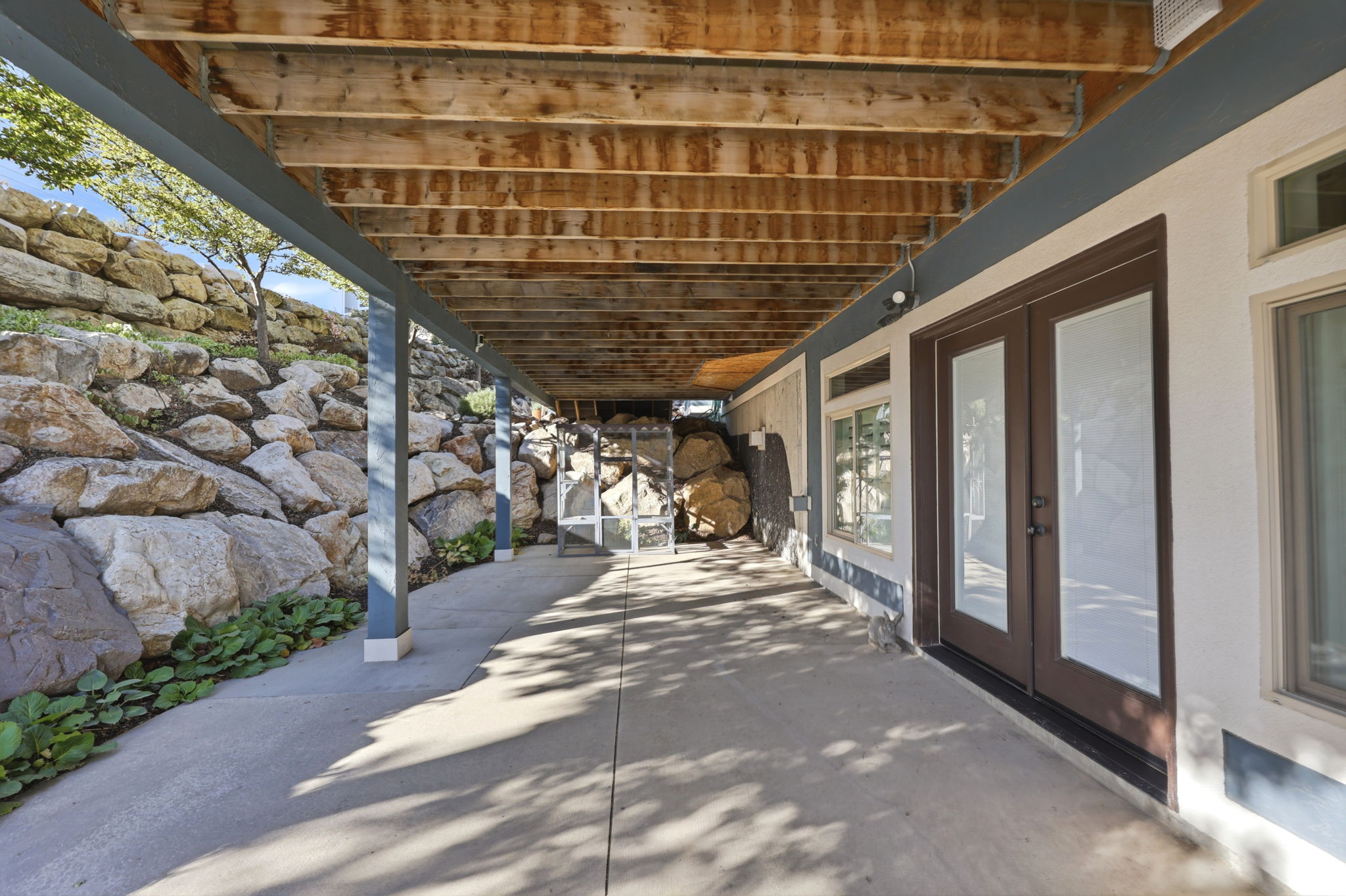 Covered patio with concrete flooring, supported by structural beams, offering direct exterior access through double French doors and a single window