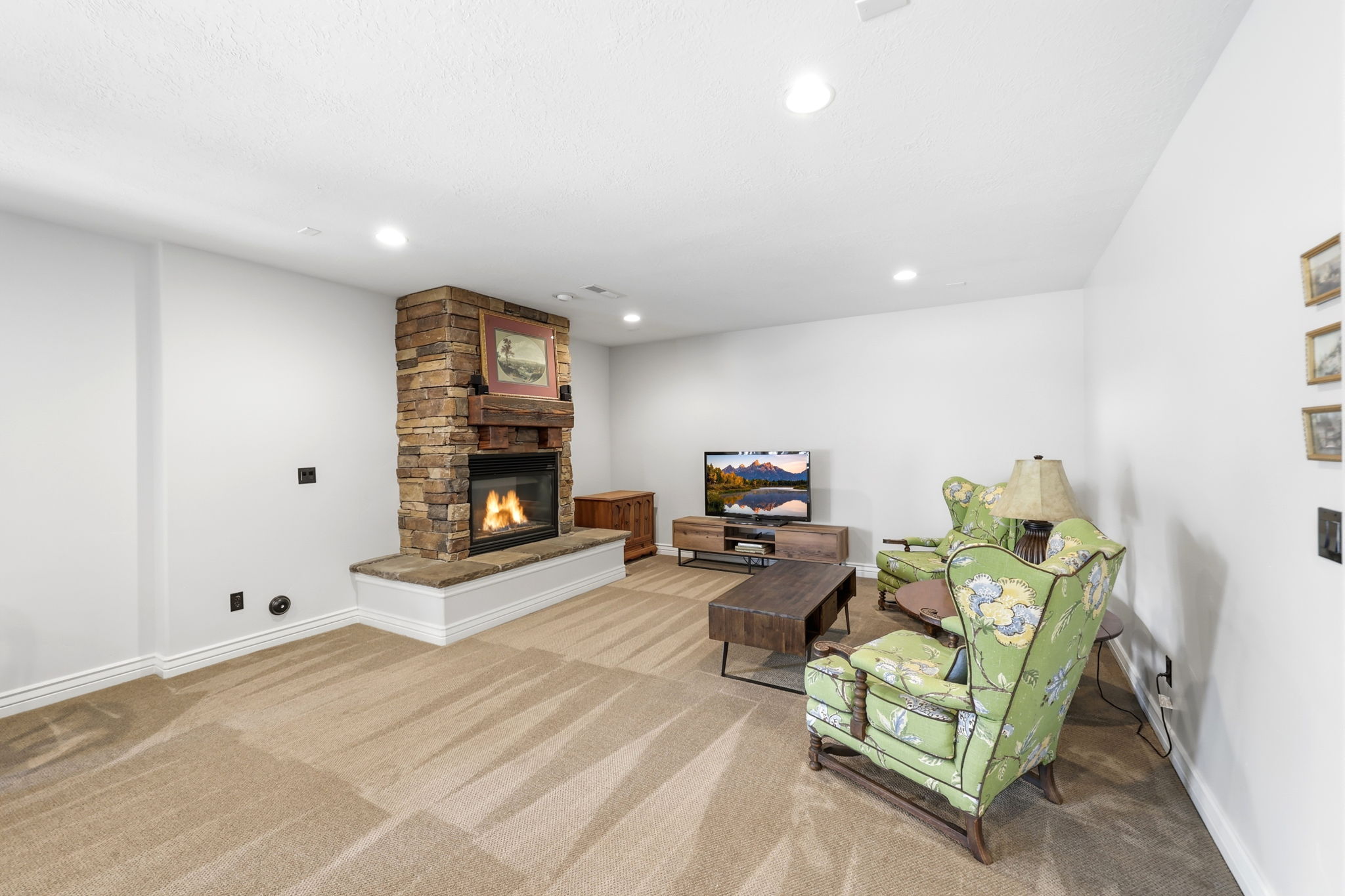 Stone-stacked fireplace with a raised hearth, wood mantle, recessed lighting, and neutral carpeting