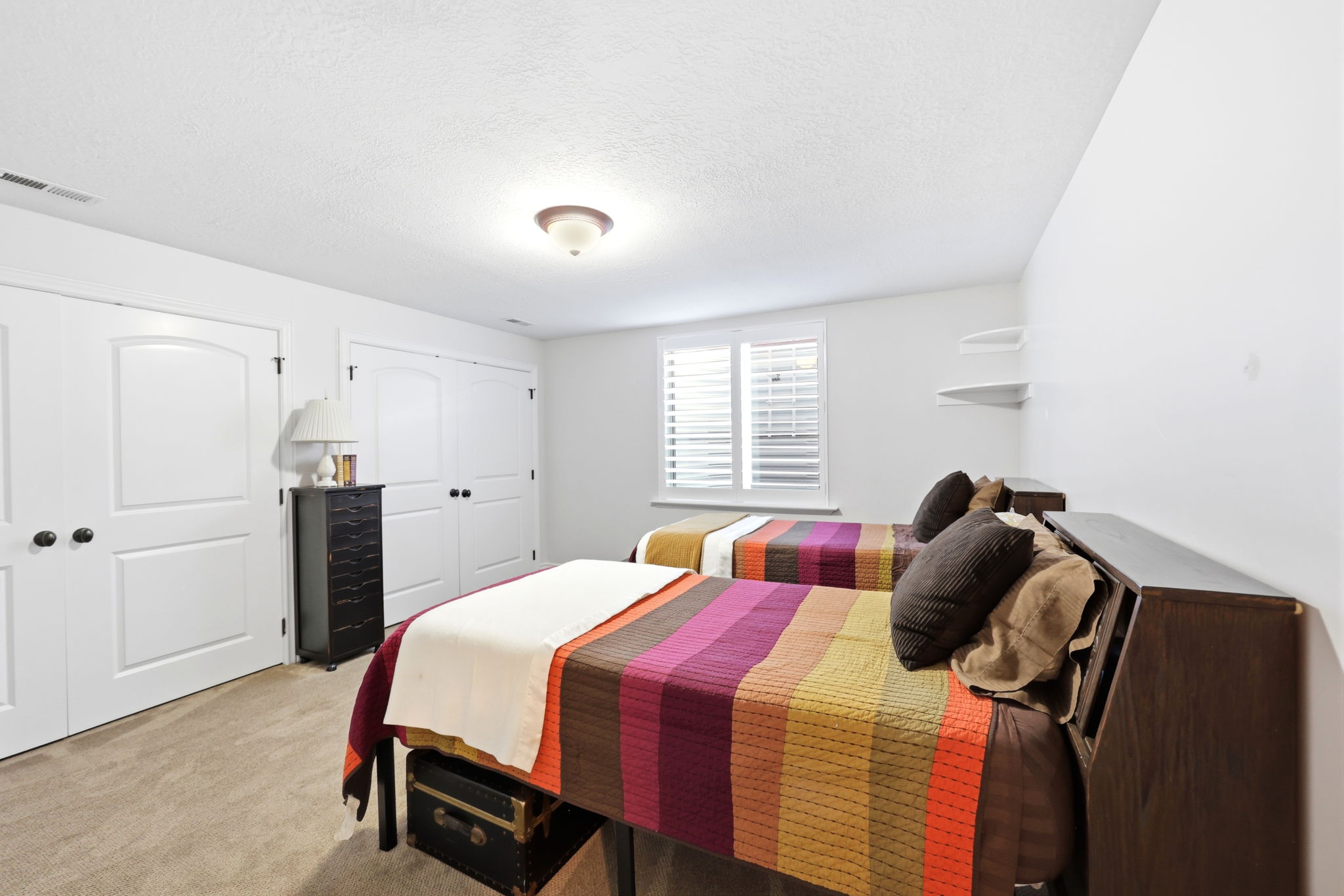 Bedroom featuring plush carpet flooring, two paneled closet doors with black hardware, and a window with white plantation shutters