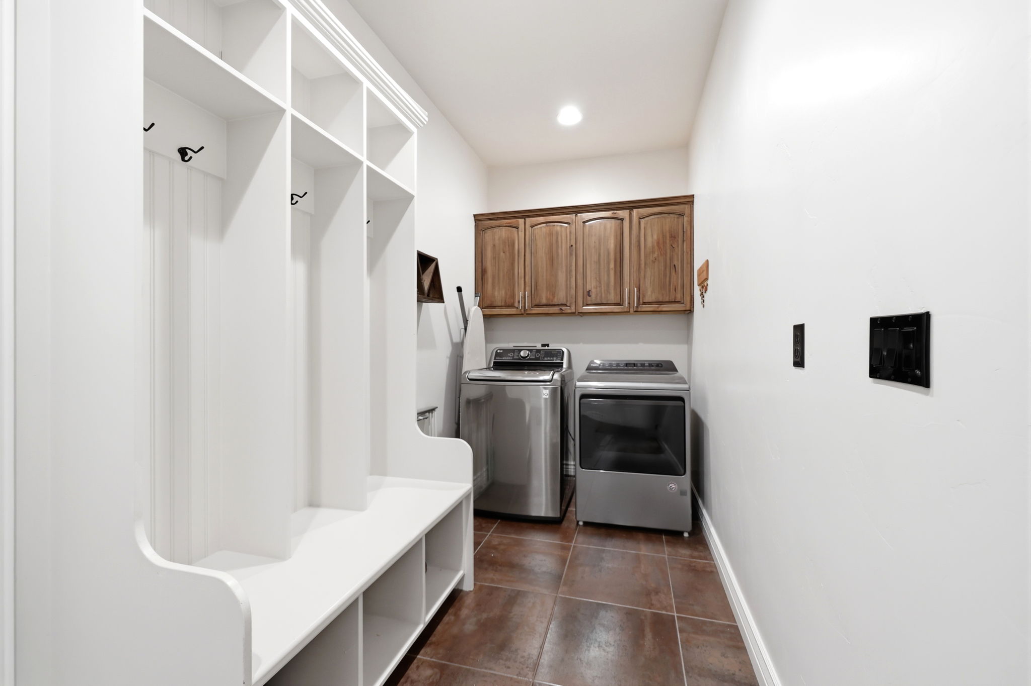 Entry area featuring a built-in white mudroom bench with cubbies and hooks, wood-finish upper cabinetry, and tile flooring