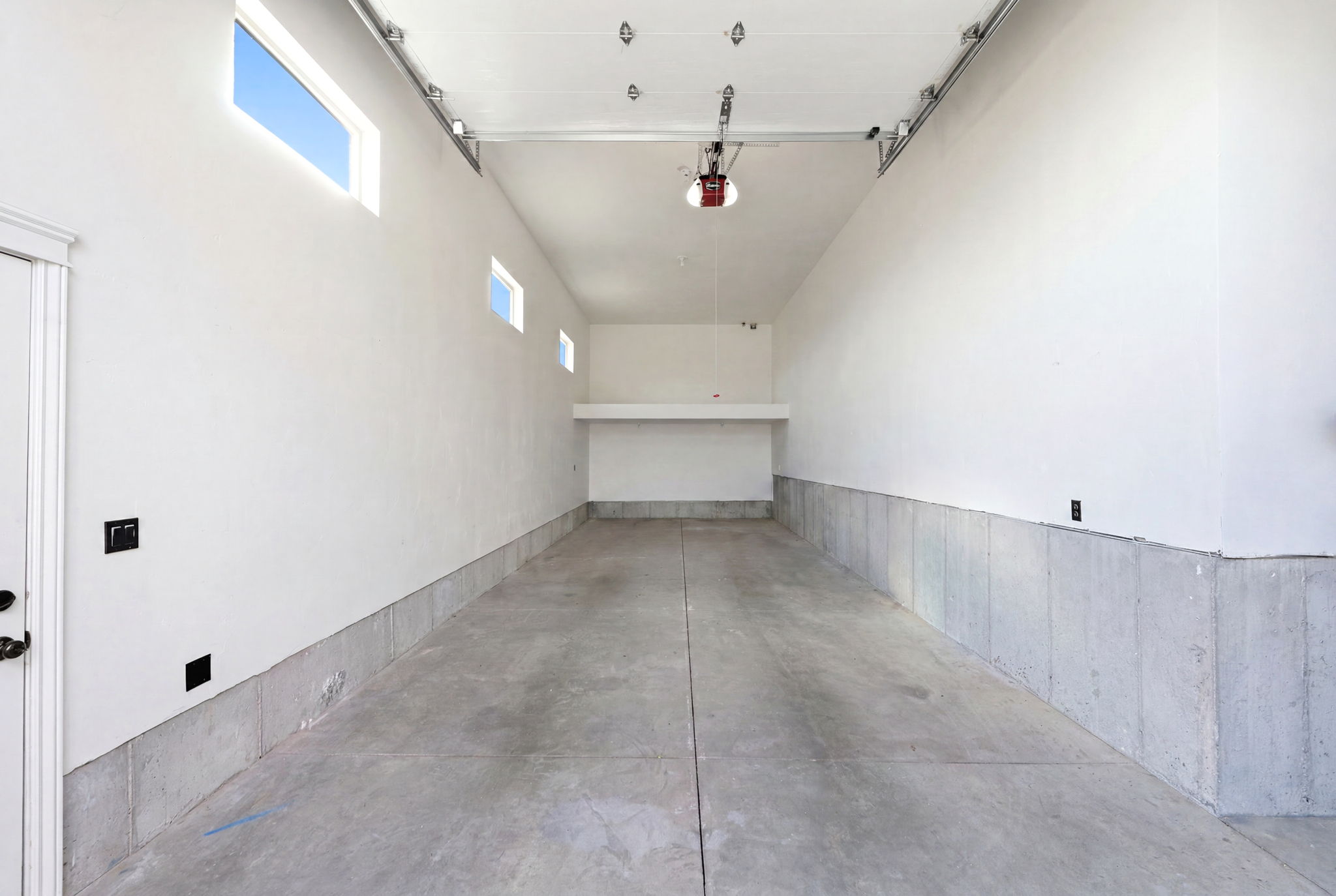 Spacious garage featuring a concrete floor, high ceilings, multiple transom windows, and a built-in storage shelf