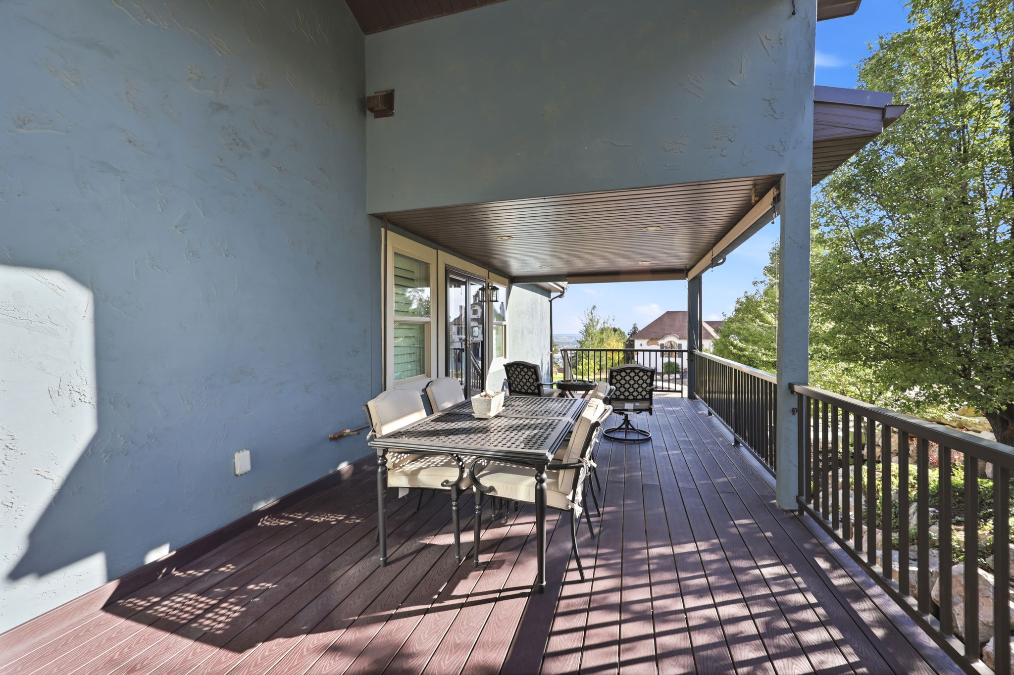 Spacious covered deck featuring composite decking, dark metal railings, and a textured stucco exterior