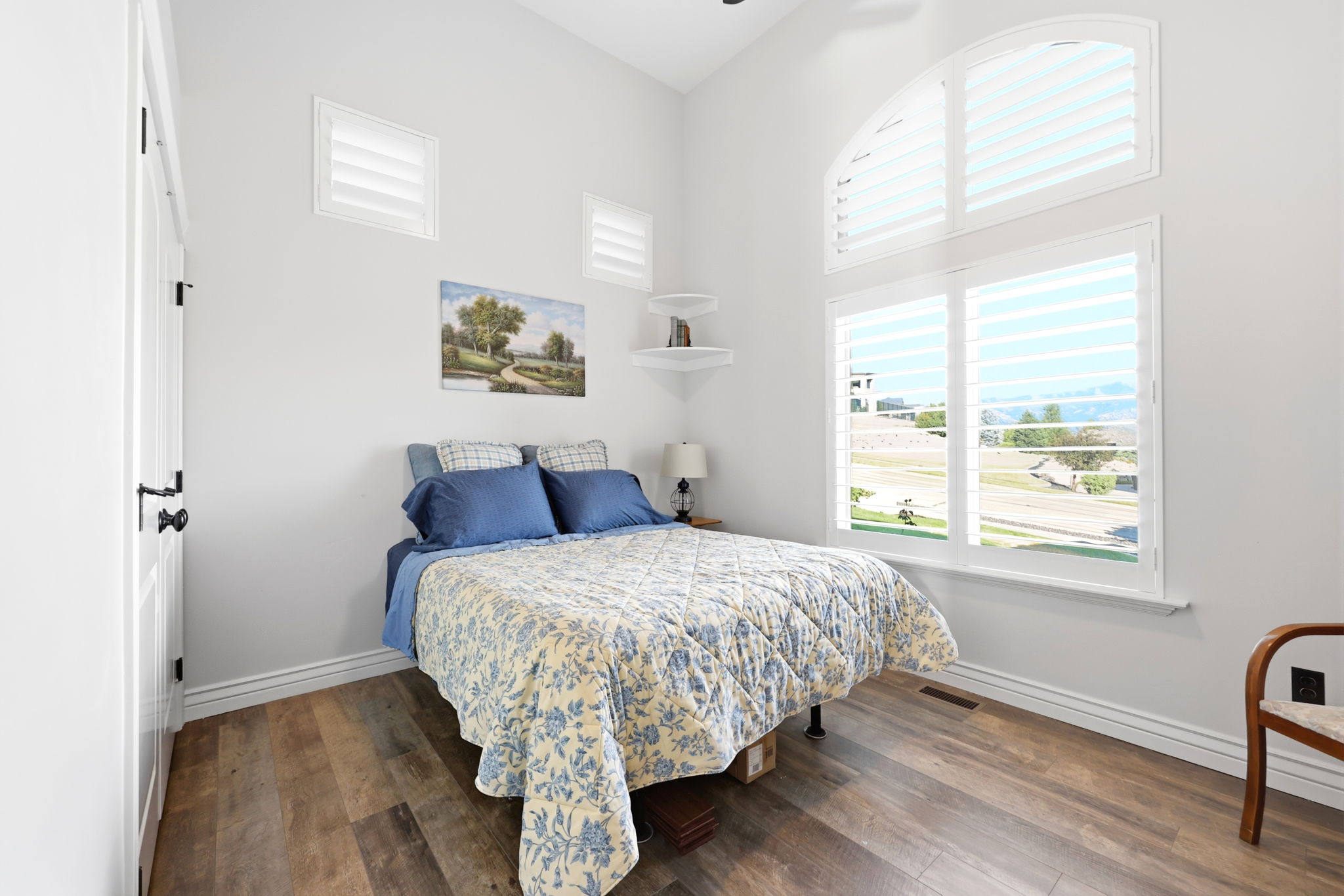 Spacious room featuring vaulted ceilings, wood-finish flooring, a large window with an arched transom, and custom plantation shutters