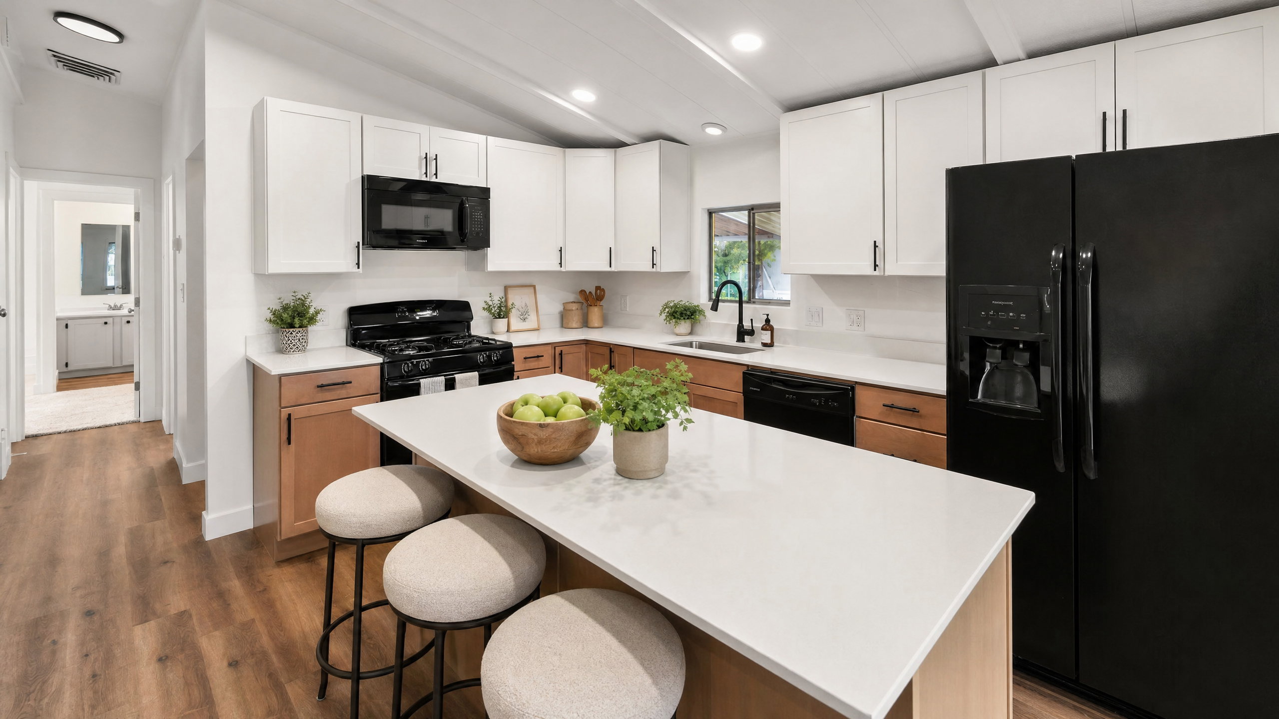 Modern kitchen featuring a central island with a light-toned countertop, two-tone cabinetry with white upper and wood-finish lower units, and black appliances