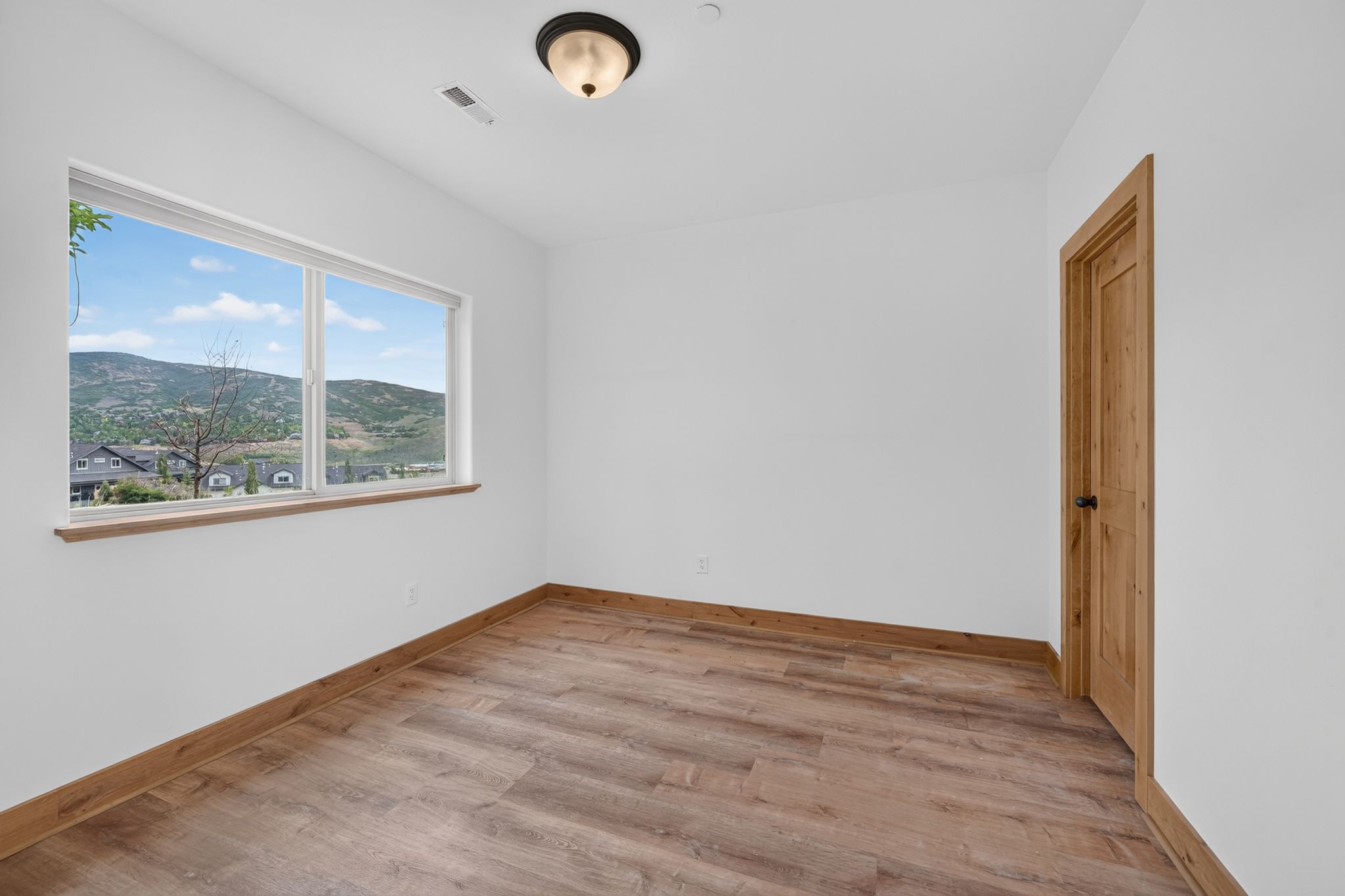 Room featuring a large picture window, wood-finish flooring, white walls, wood trim, and a wood panel door