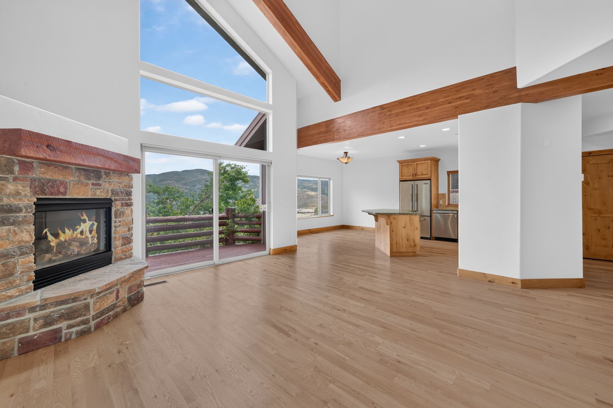Open-concept living space featuring a stone-faced fireplace with a wood mantel, wood-finish flooring, and vaulted ceilings with exposed wood beams