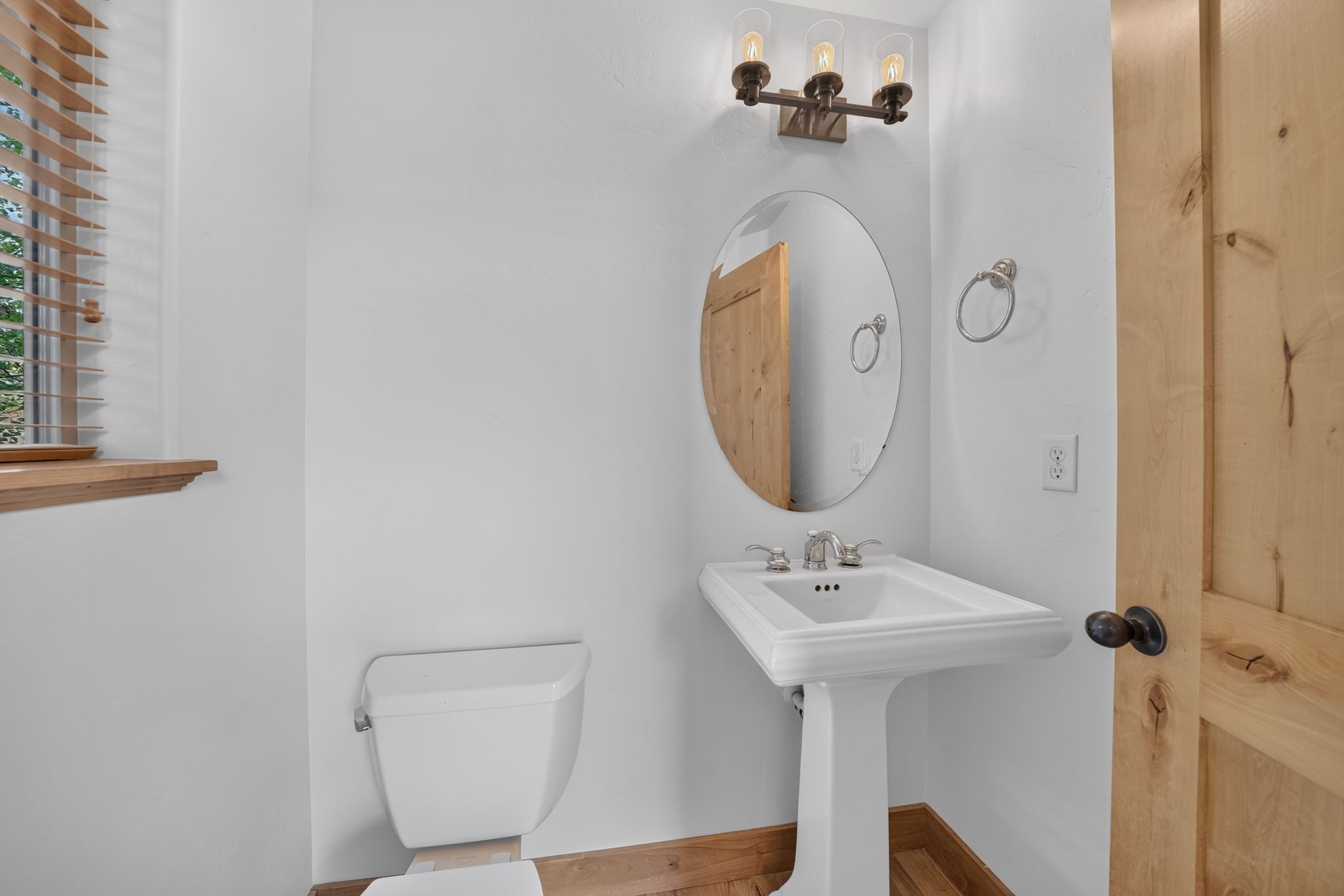 Pedestal sink with chrome faucet, oval mirror, and wall-mounted vanity lighting