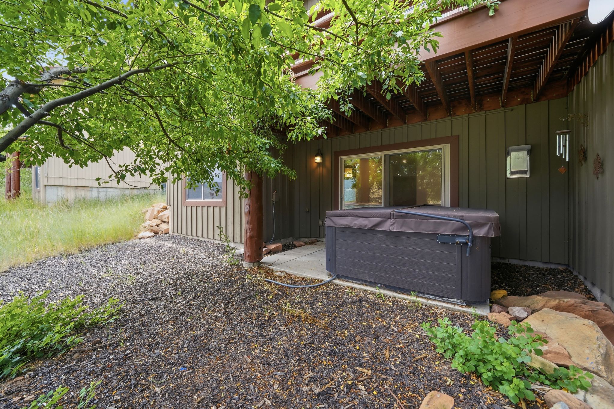 Outdoor spa situated on a concrete patio beneath a wooden deck, featuring a sliding glass door entry to the interior