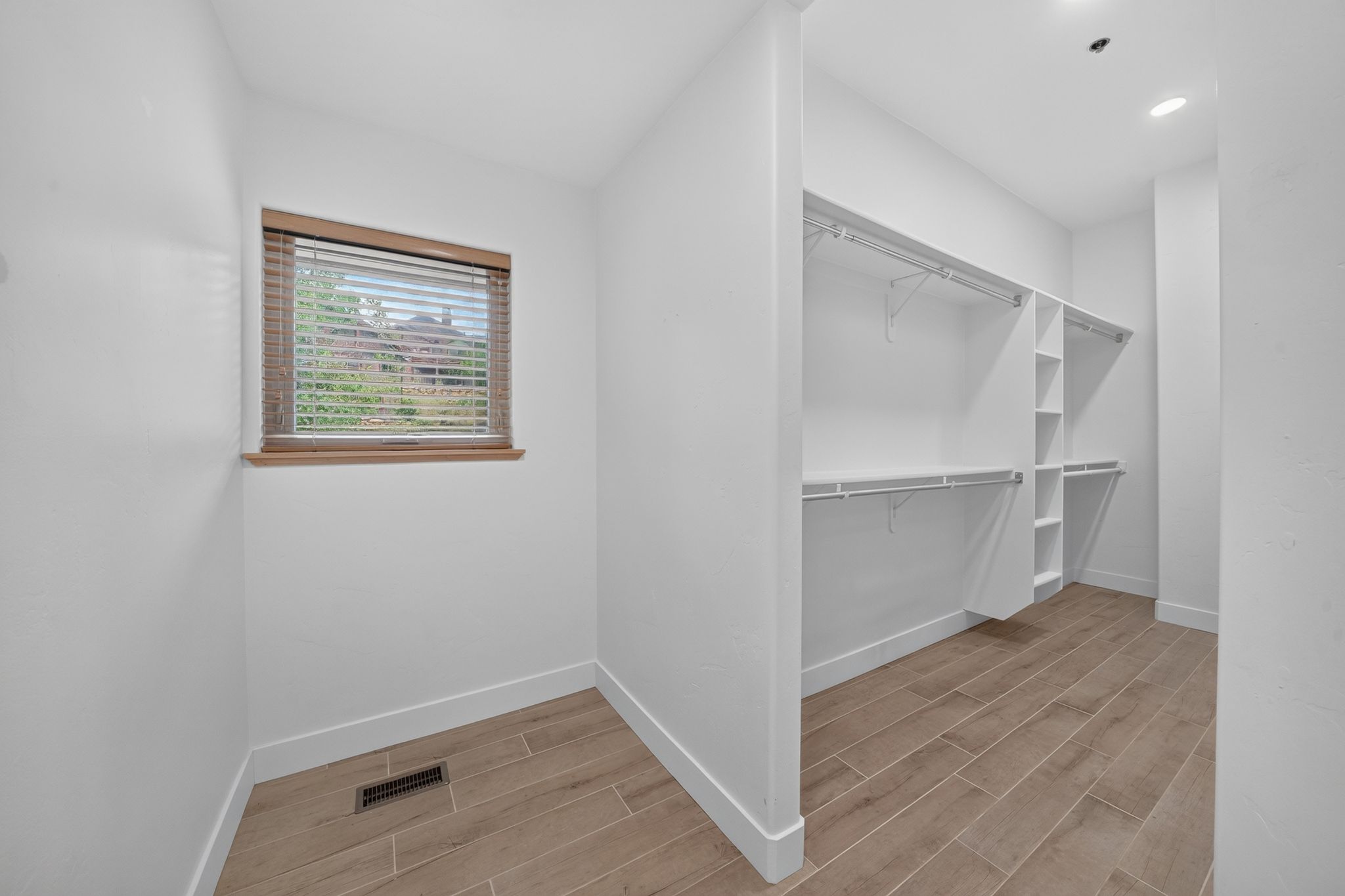 Spacious walk-in closet featuring wood-finish flooring, white walls, and a window with wood blinds