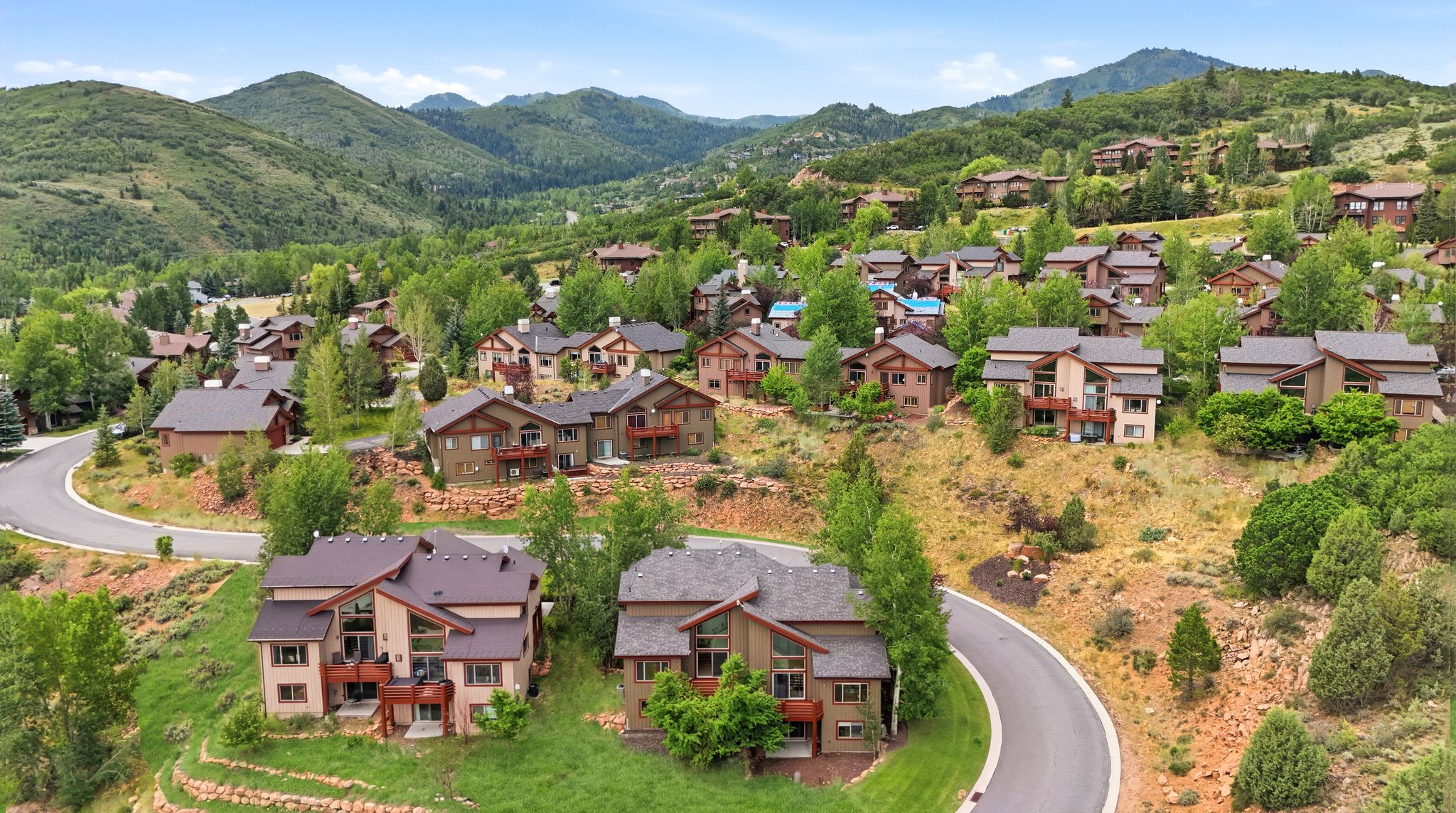 Mountain community featuring multiple multi-story residences with diverse architectural styles, mature trees, and paved roads