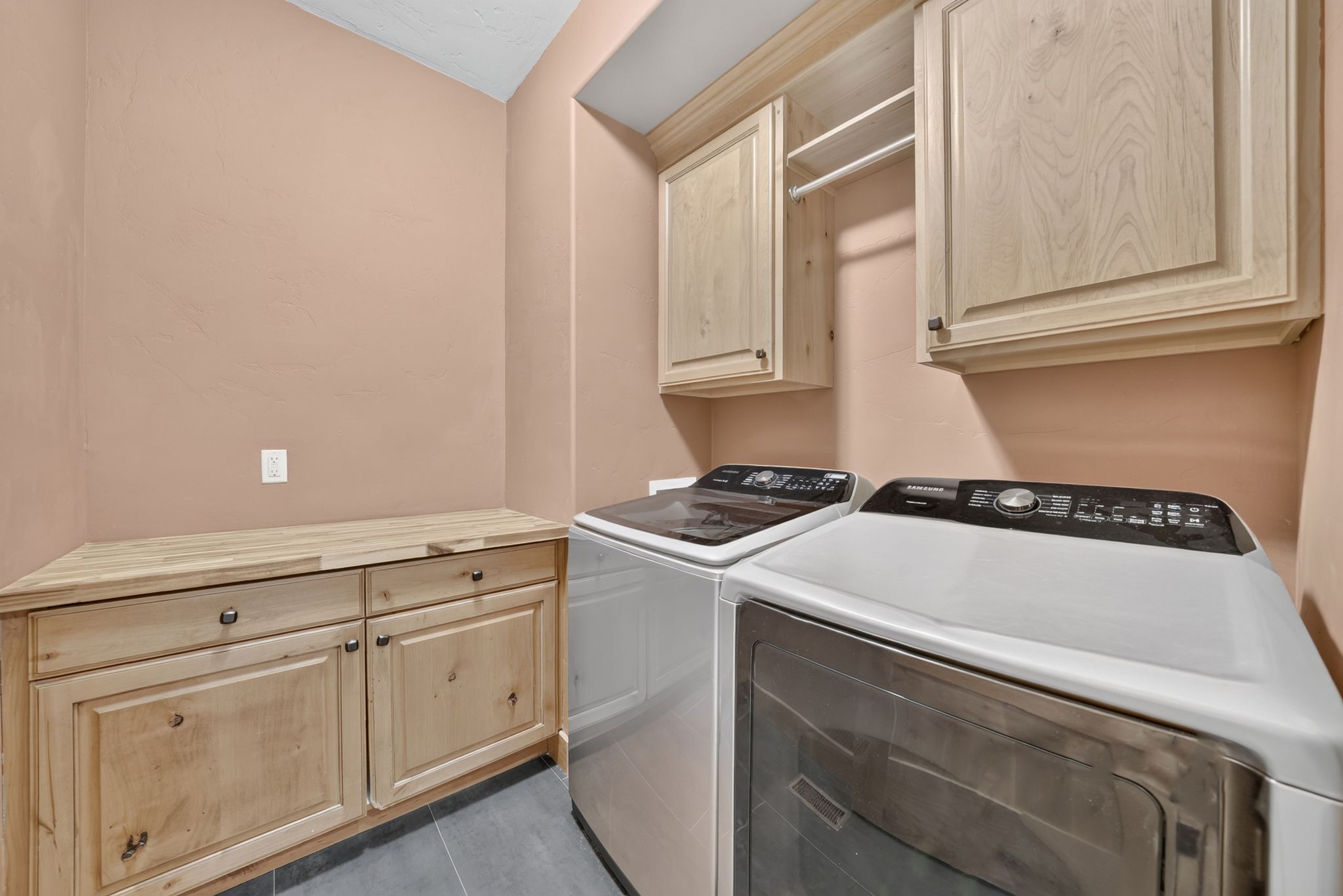 Laundry area featuring light wood cabinetry, integrated countertop space, a built-in hanging rod, and dark gray floor tiling