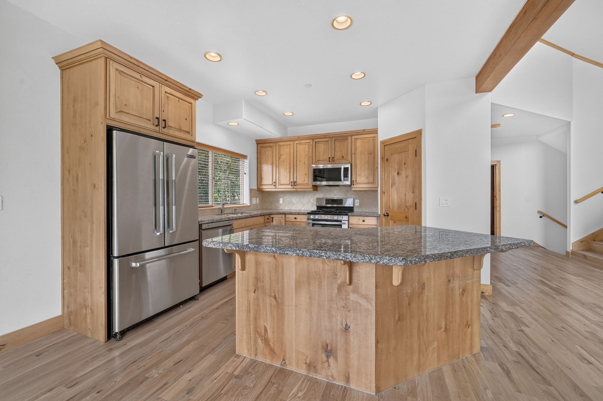 Contemporary kitchen featuring stainless steel appliances, light wood-finish cabinetry, a large center island with a granite countertop, and recessed lighting