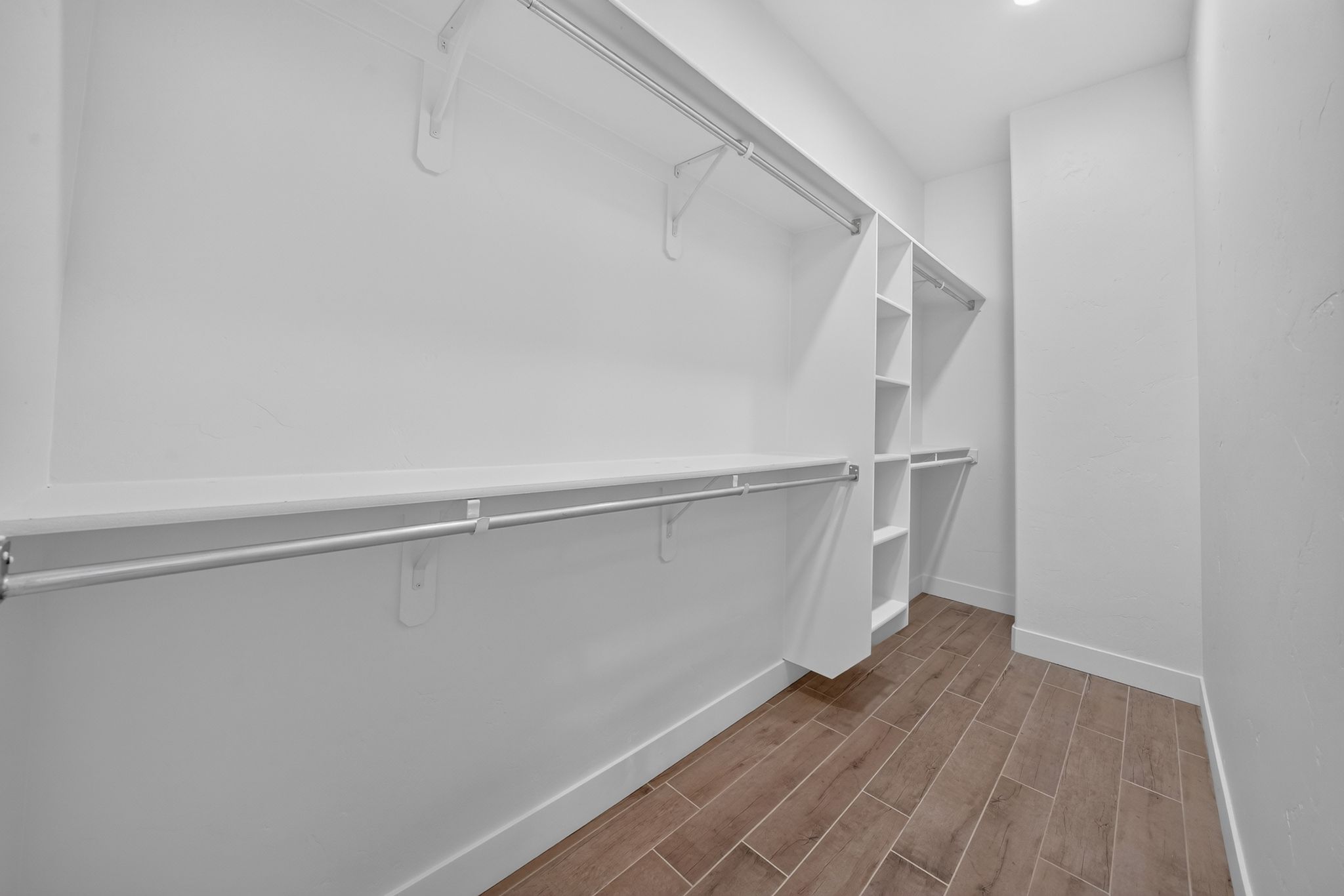 Walk-in closet featuring built-in shelving, multiple hanging rods, and wood-finish flooring