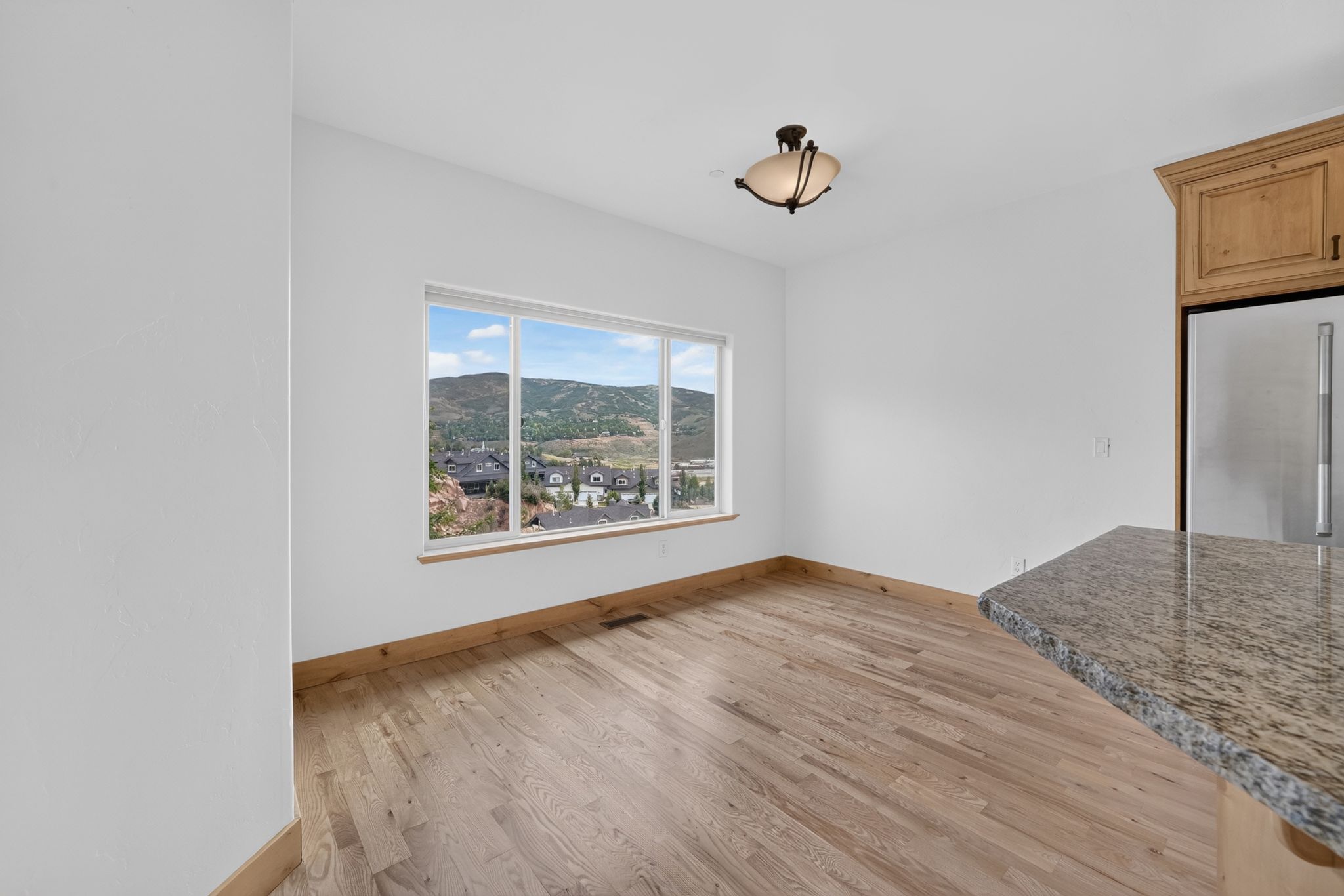 Bright interior space featuring a large picture window, wood-finish flooring, and a contemporary ceiling light fixture