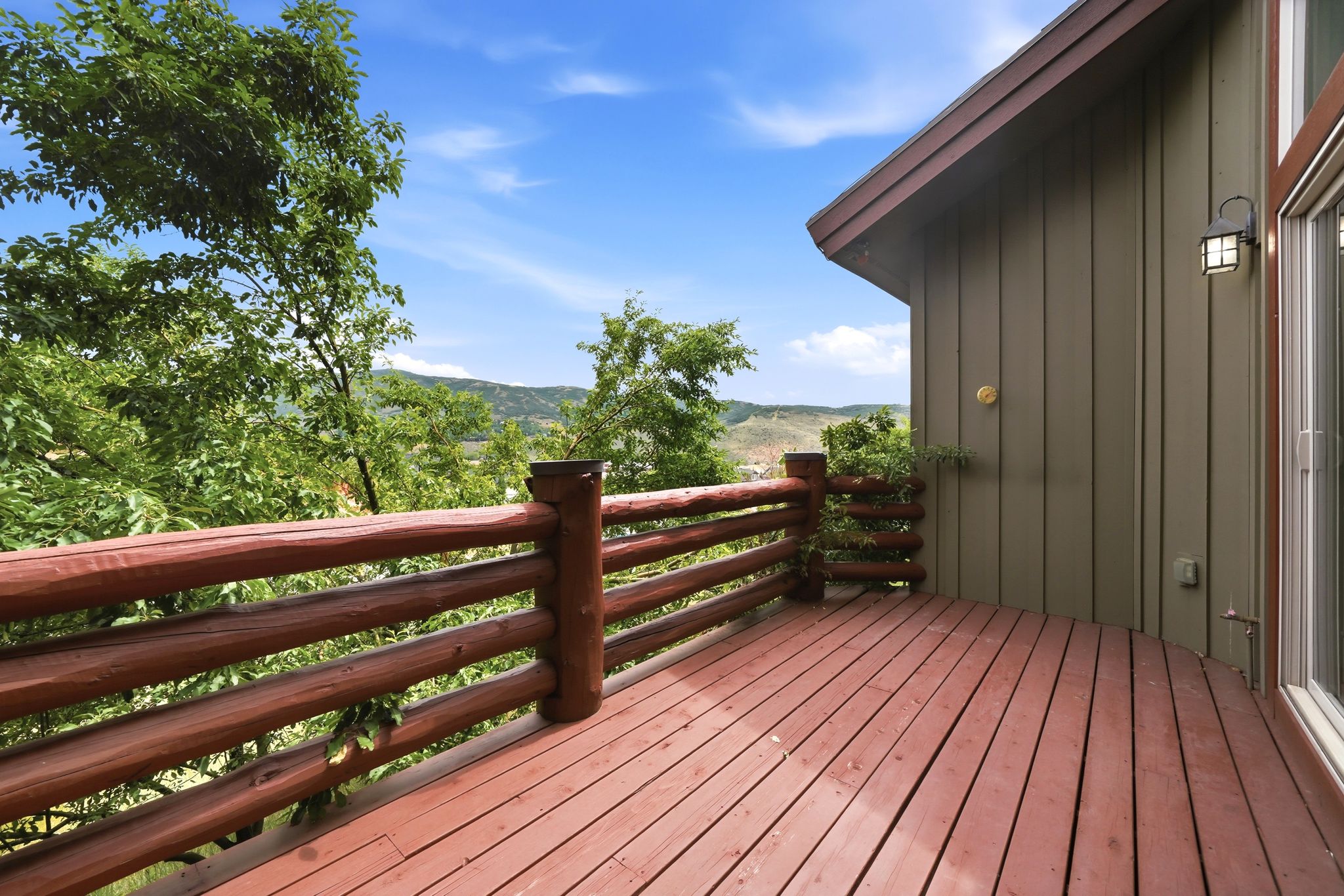 Spacious outdoor deck with rich wood flooring, featuring a rustic log railing and an exterior wall with vertical paneling