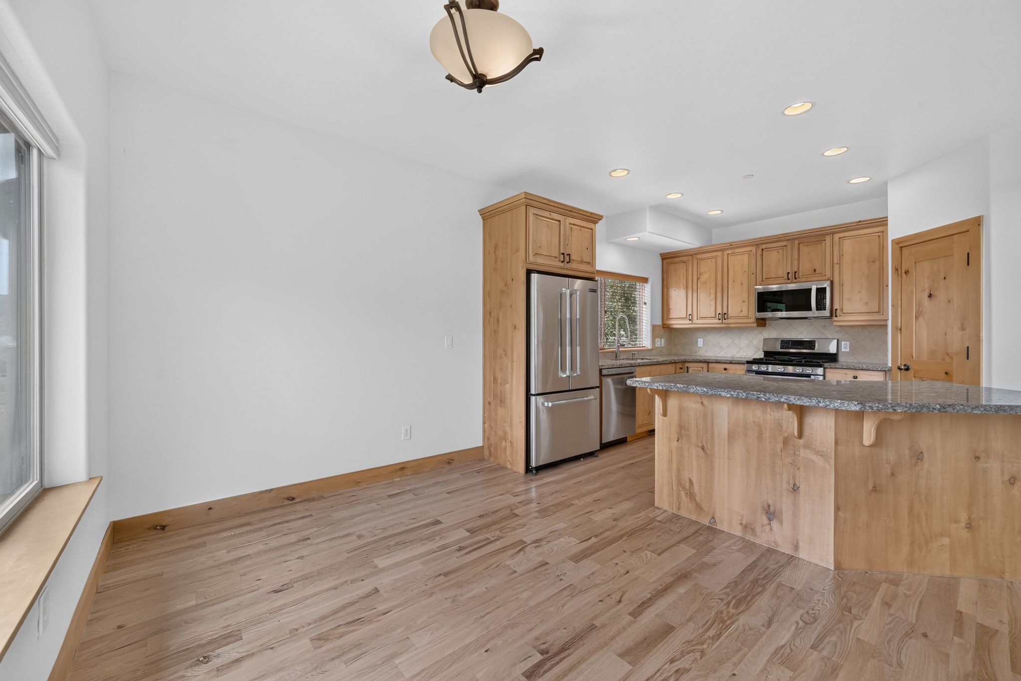 Open-concept kitchen and dining area featuring wood-finish flooring, light wood cabinetry, stainless steel appliances, granite countertops, and recessed lighting