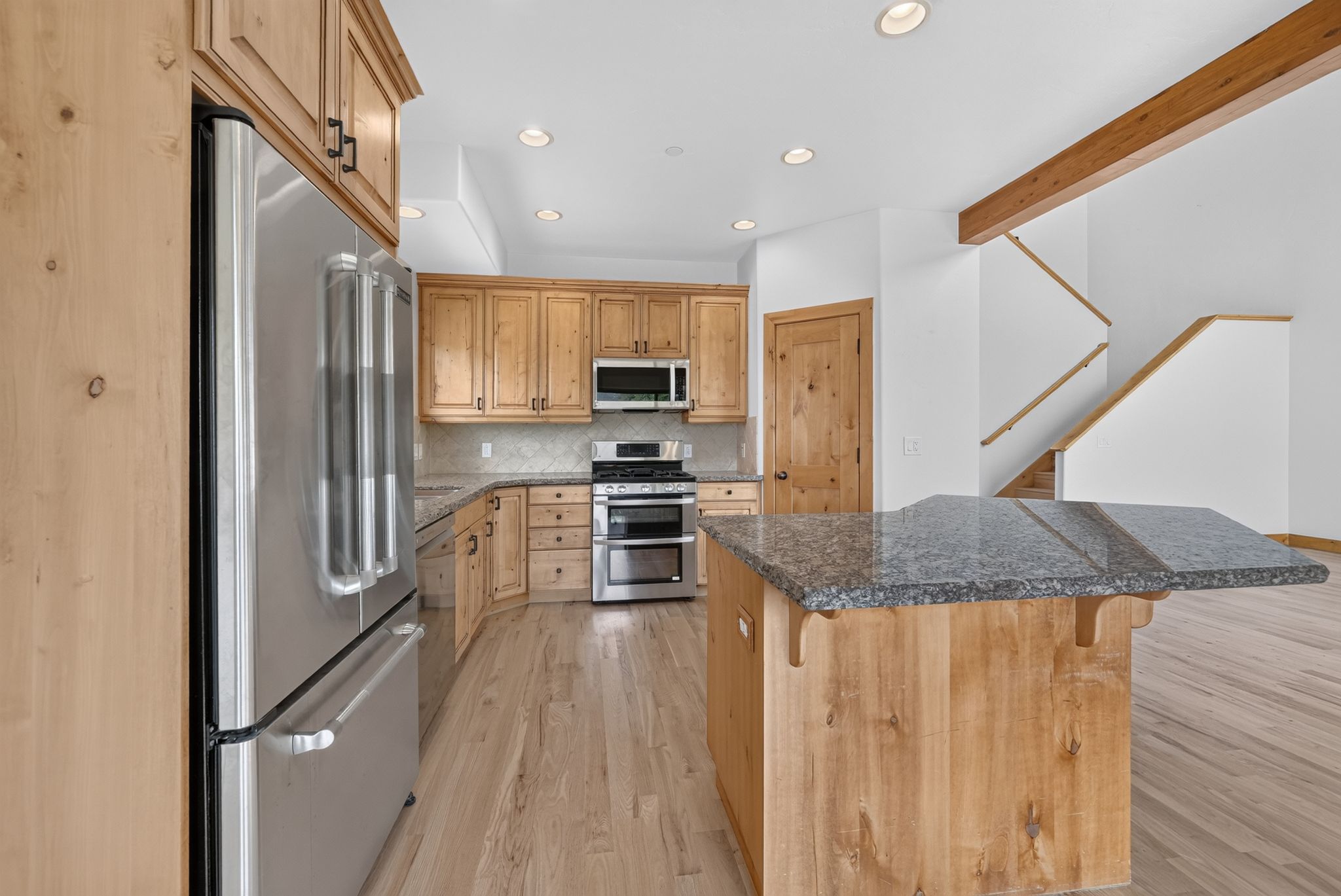 Kitchen featuring stainless steel appliances, wood cabinetry, granite countertops, and wood-finish flooring