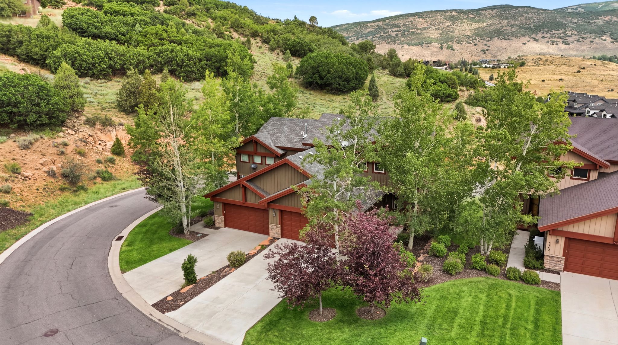 Mountain-style residence featuring a two-car garage with wood-finish doors, a concrete driveway, and a manicured lawn