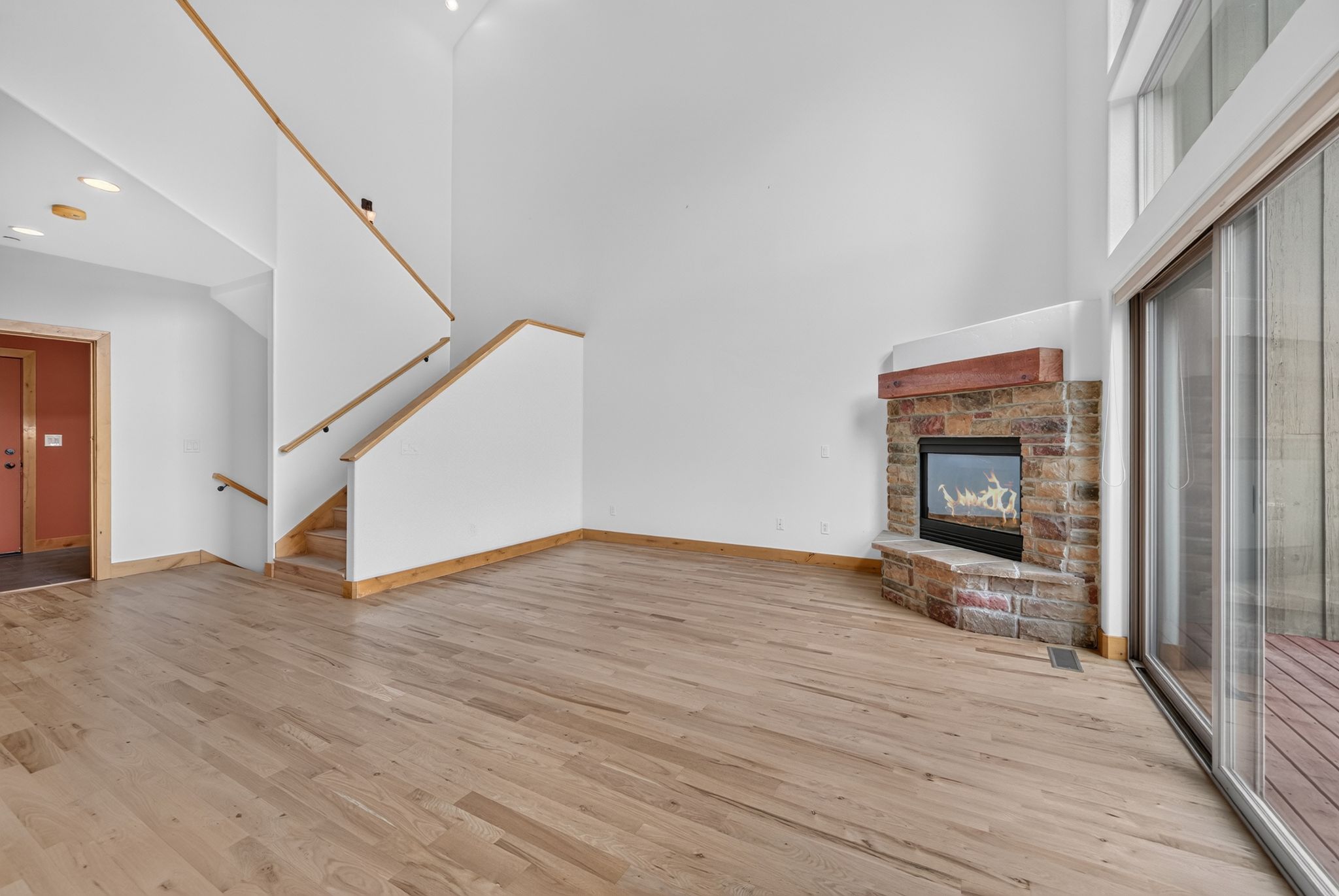 Spacious living area featuring wood-finish flooring, a stone fireplace with a wood mantle, and high ceilings