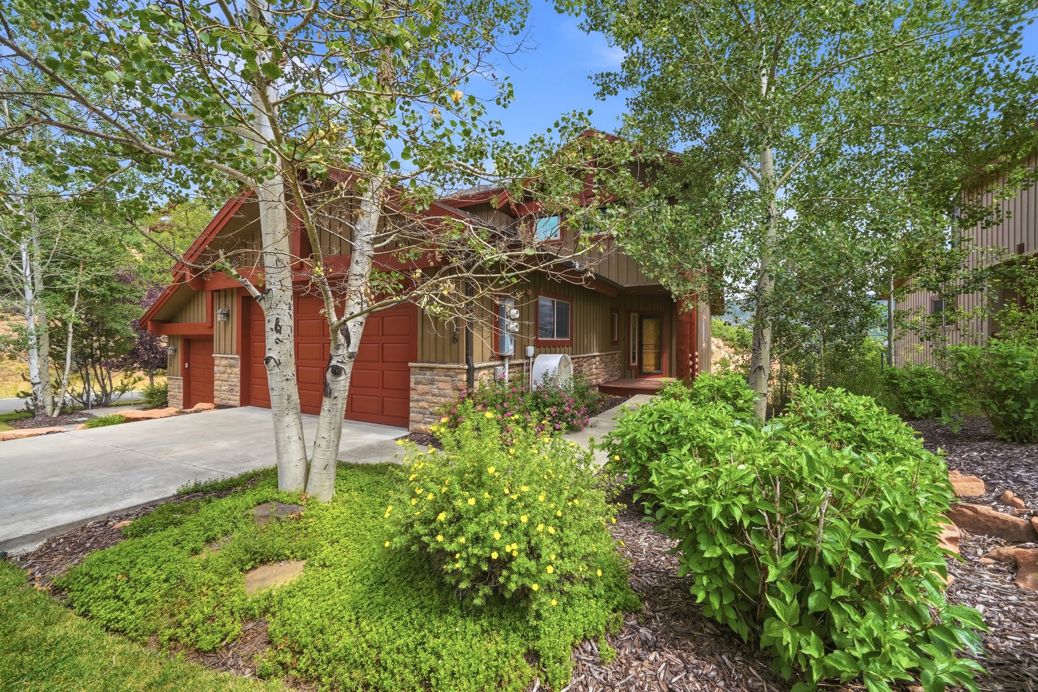 Rustic-style exterior featuring a multi-toned facade, attached two-car garage, mature landscaping, and a concrete driveway