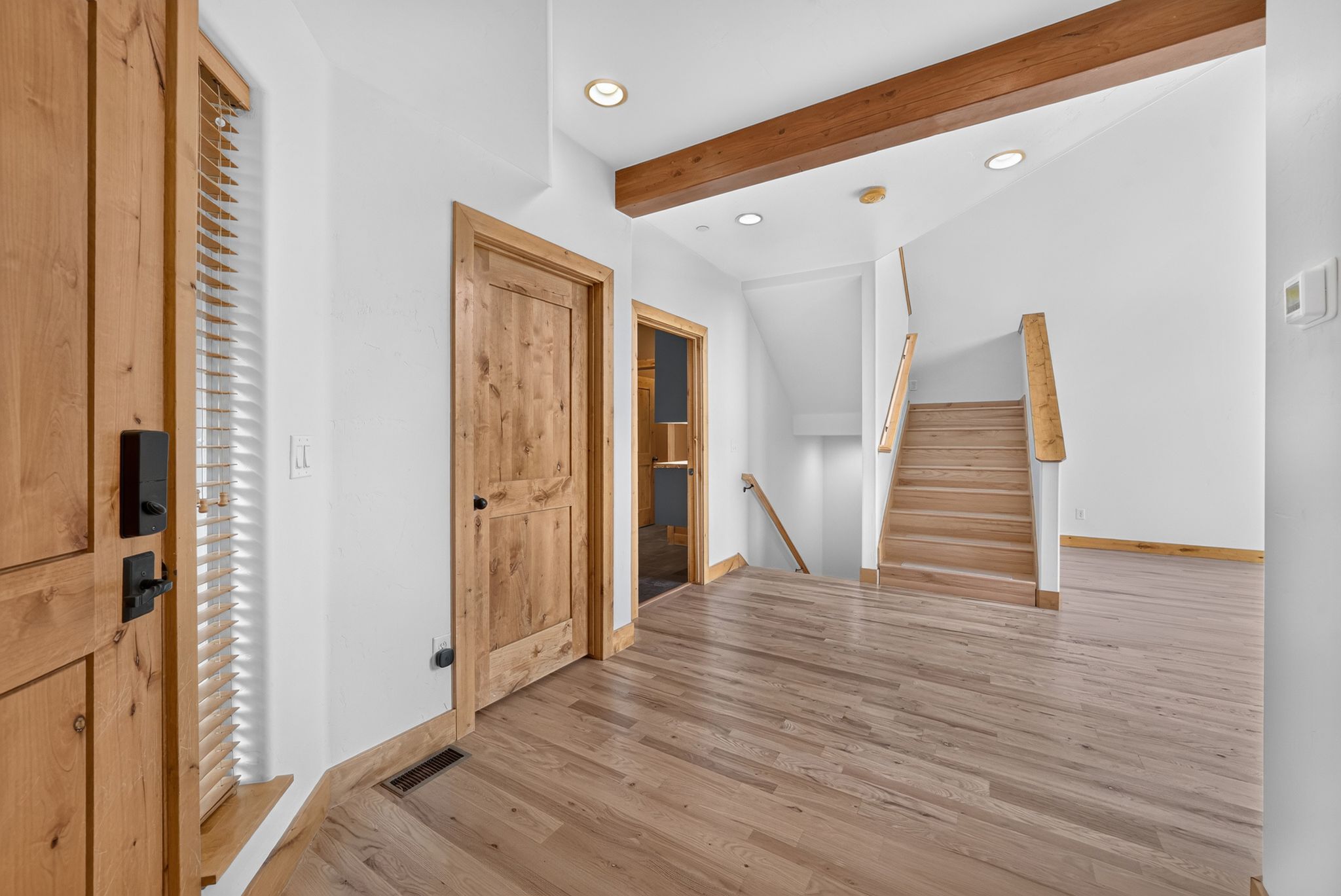 Entryway with wood-finish flooring, a solid wood door with black hardware, and a staircase featuring wood treads and railings